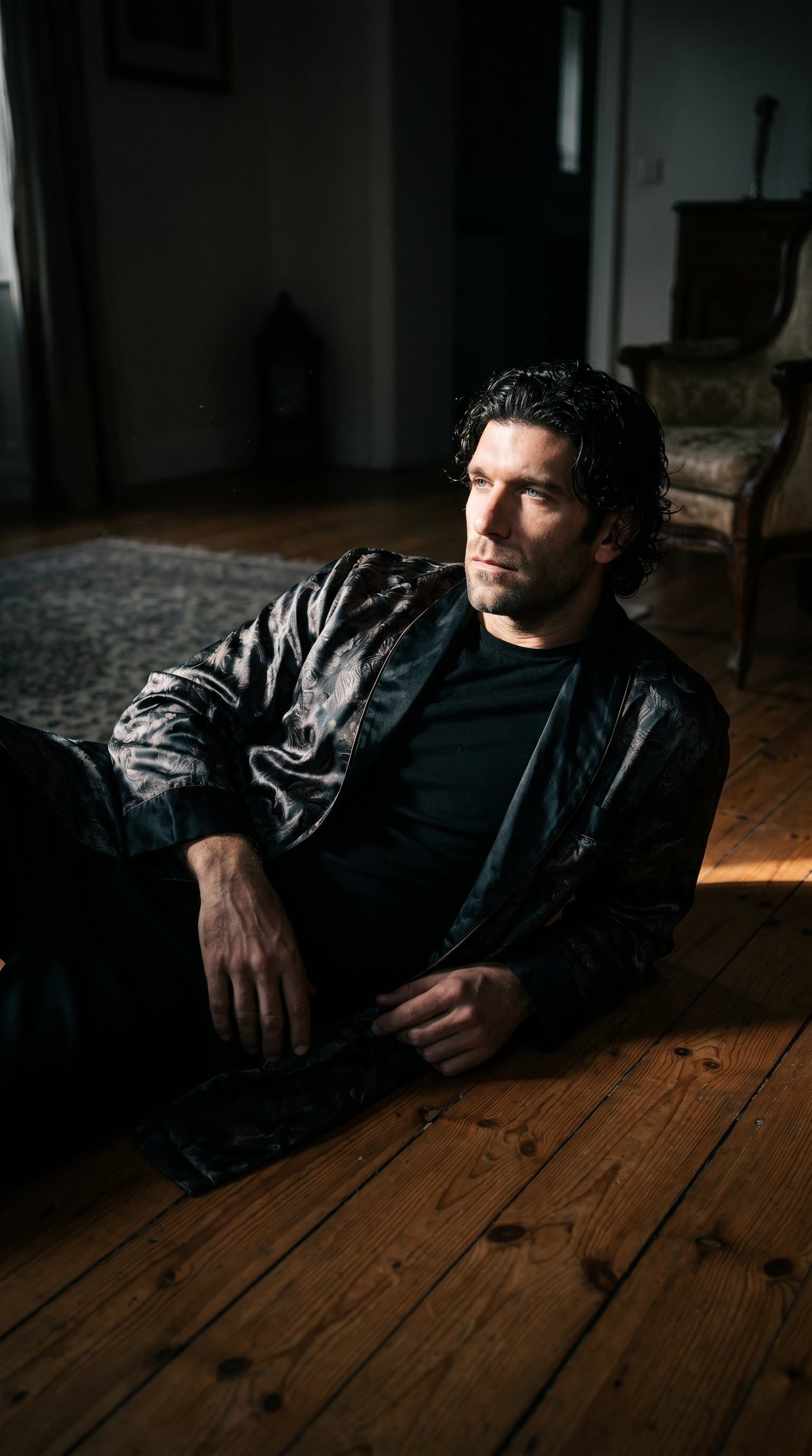 man reclining on a hardwood floor, wearing a silky robe with dramatic, low-key lighting