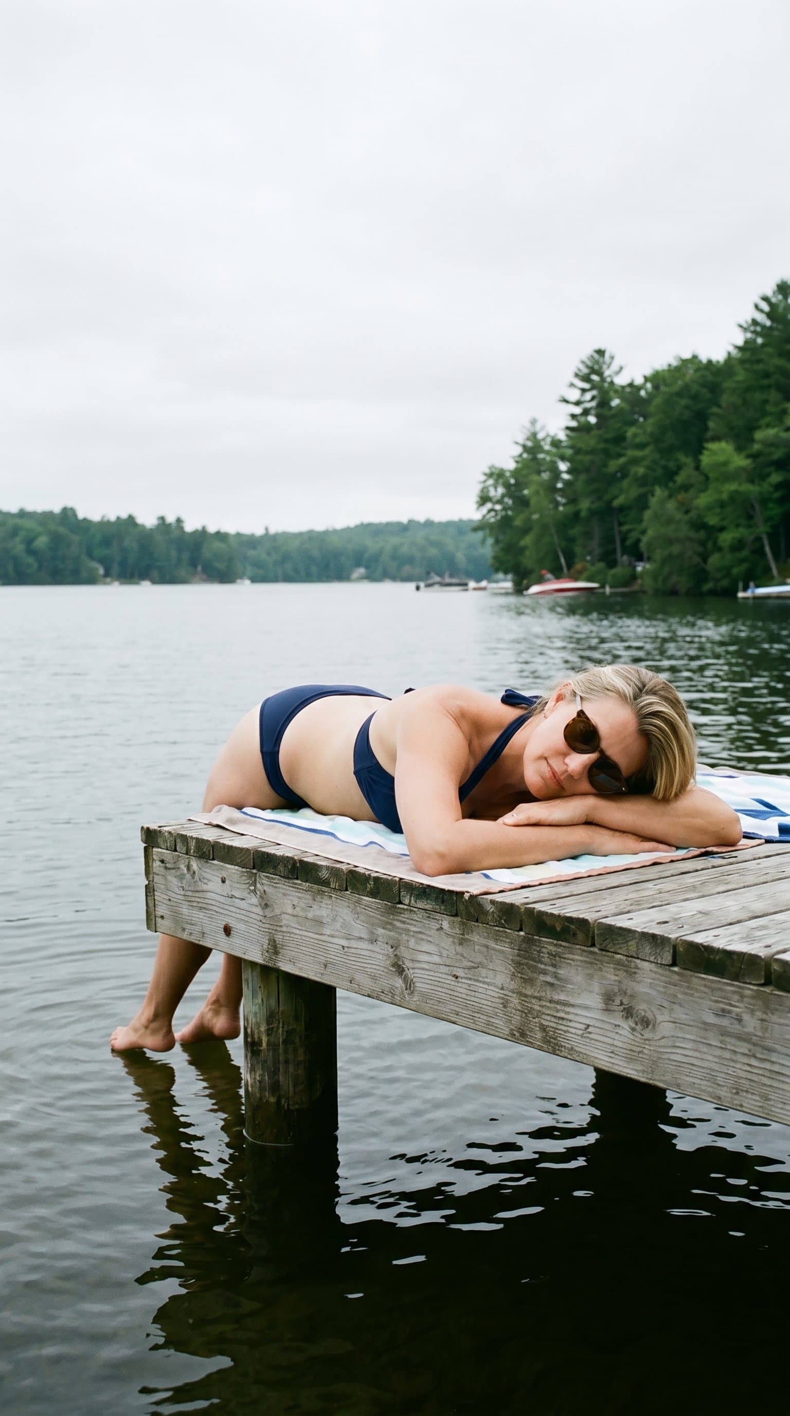 woman in a halter bikini, laying on a dock with their feet in the water, under the soft light of an overcast sky