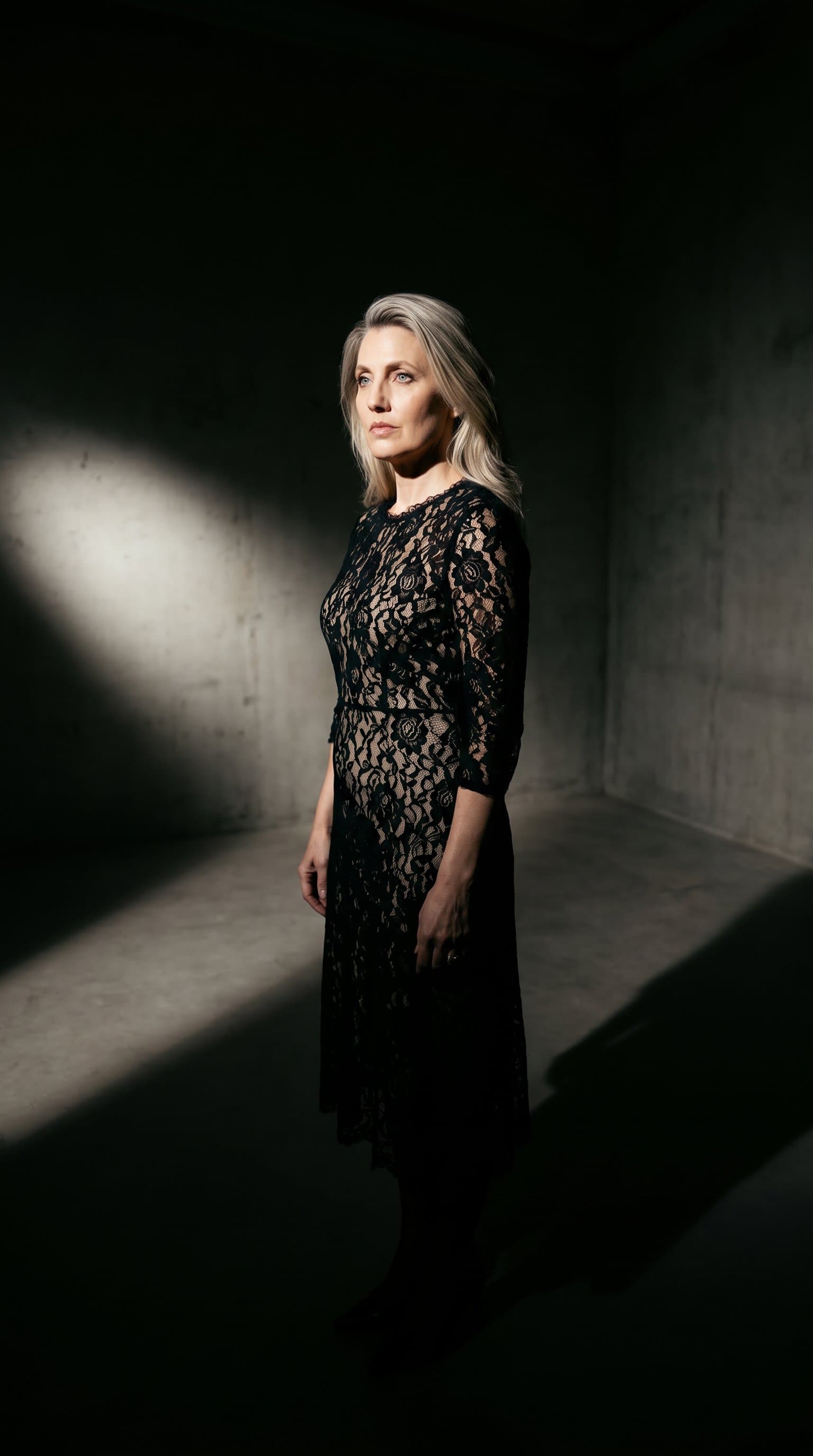 woman in an empty room, dressed in a lacy outfit and lit by a single light source casting dramatic shadows