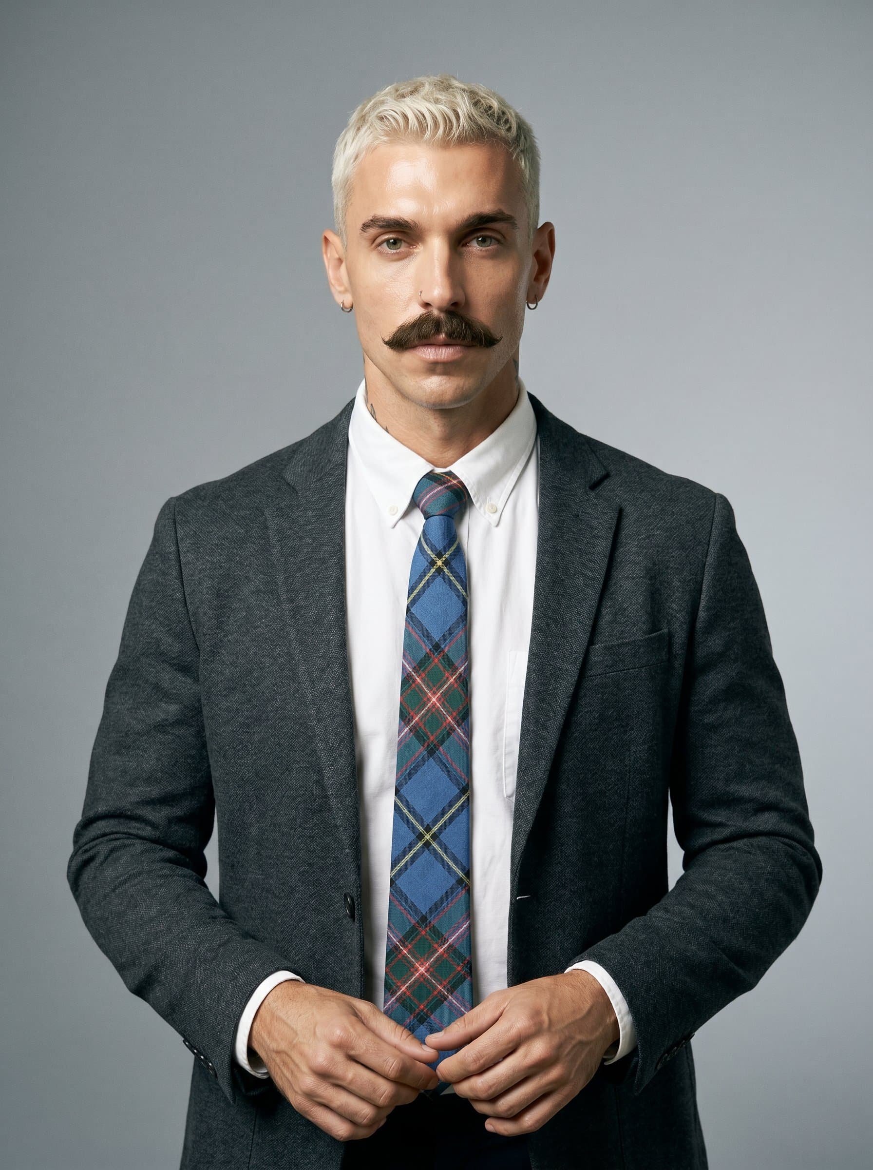 A self-assured in a plaid tie and white shirt, standing confidently. Neutral grey backdrop with balanced lighting, emphasizing the βs analytical prowess and solution-oriented approach.