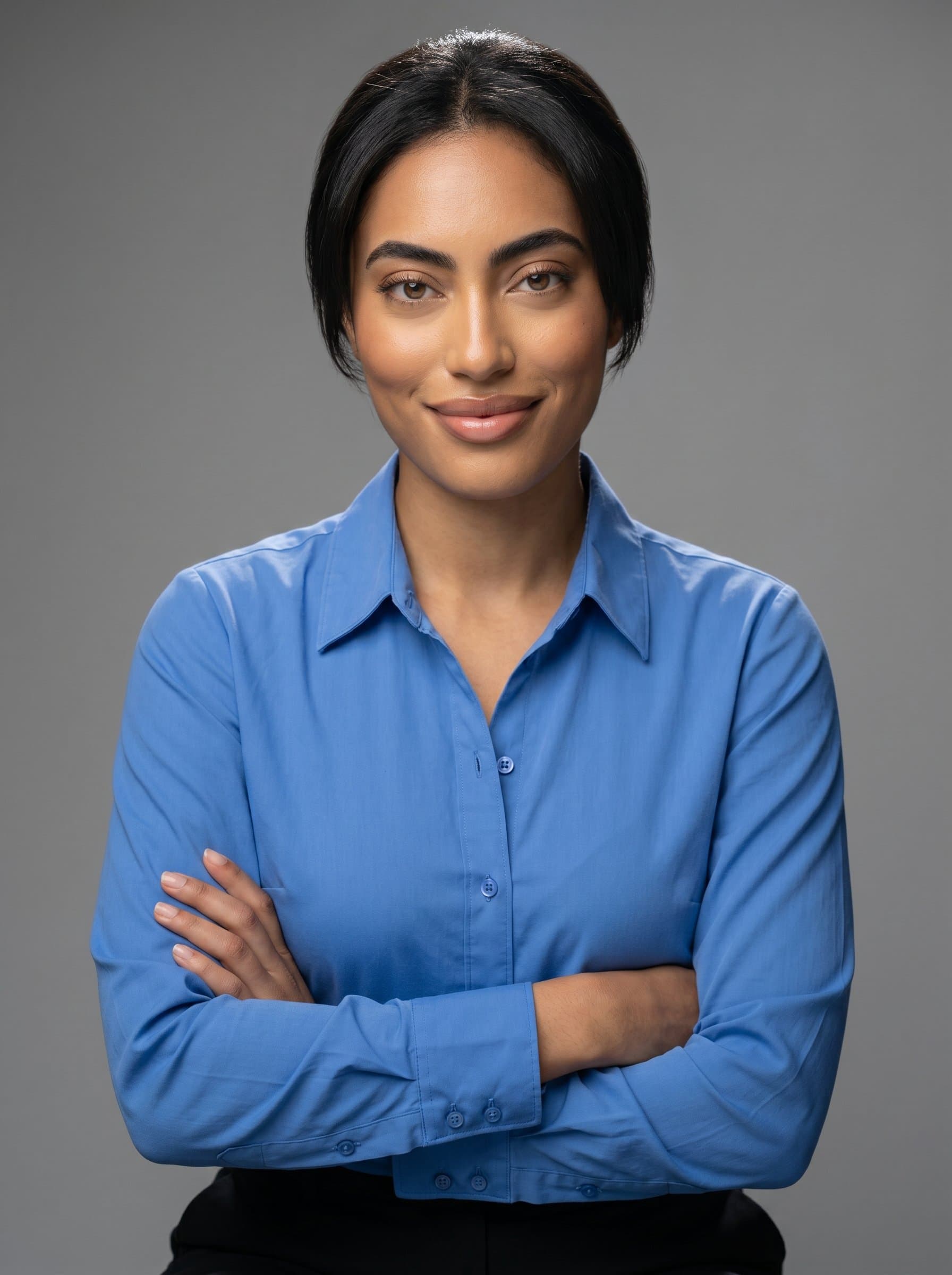 A professional looking dressed in a crisp blue shirt, seated with arms crossed, exuding confidence. Neutral grey background, gentle overhead lighting highlighting the 's facial features, conveying trust and competence.