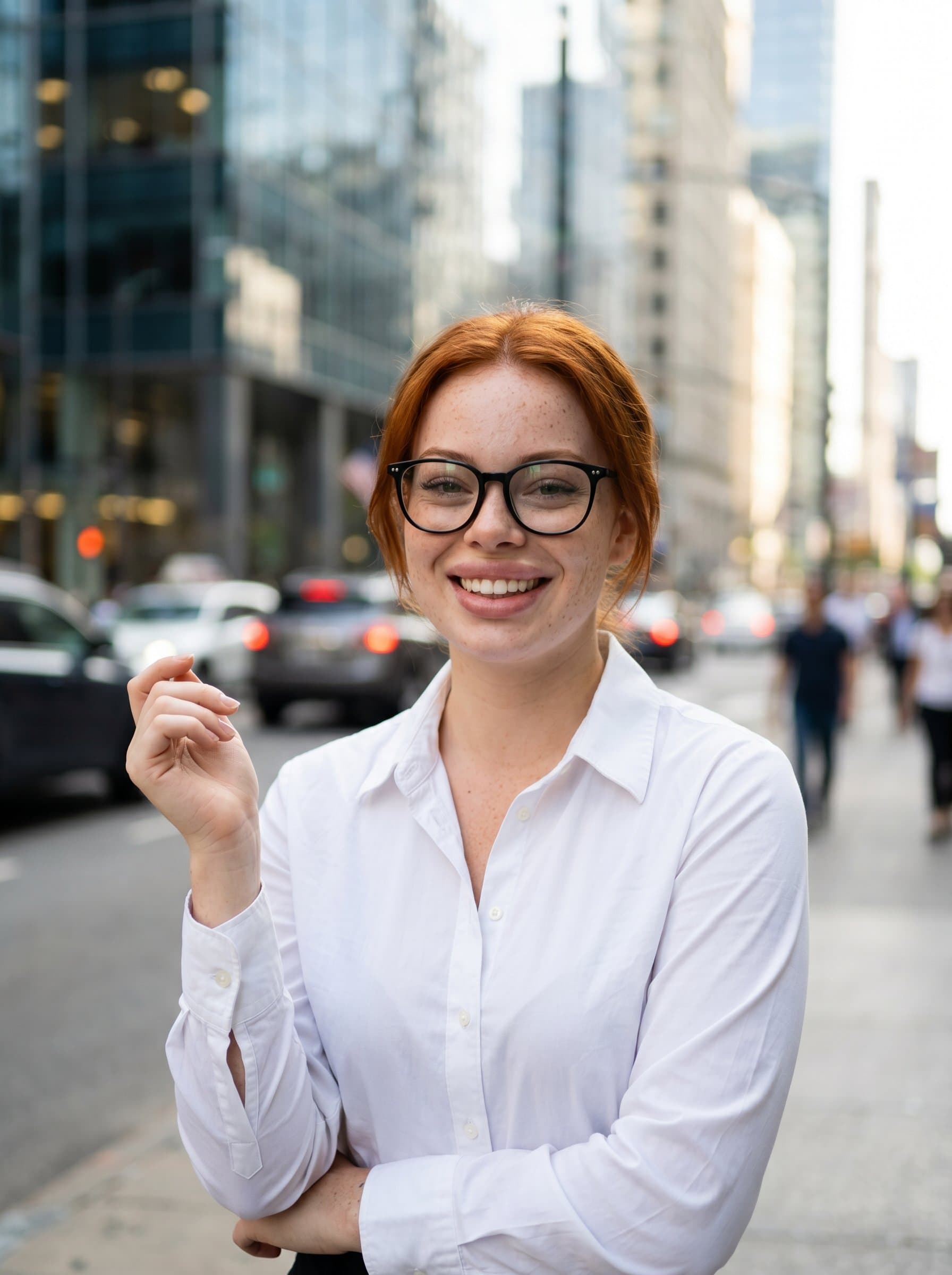 wearing glasses, crisp white shirt, smiling confidently, with an artfully blurred urban street background, capturing a dynamic presence suitable for a marketing executive.