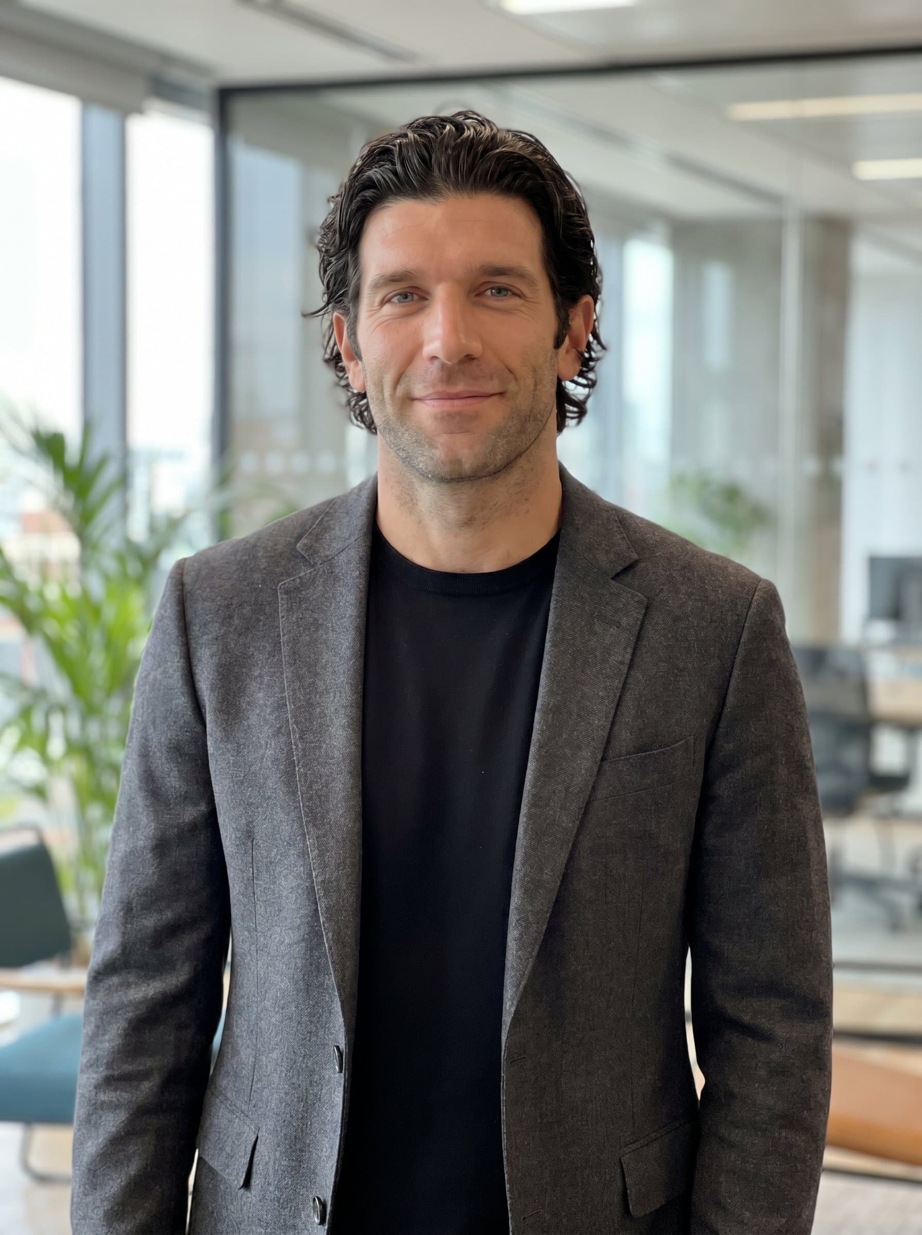 wearing a tailored blazer over a minimalist shirt, smiling subtly, with a soft-focus backdrop of a modern office. Crisp, detailed image projecting approachability and innovative spirit for a creative agency professional.
