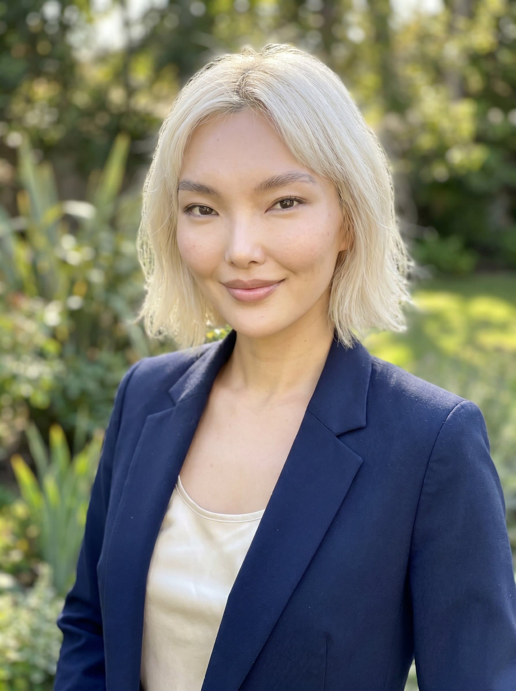 in business casual attire, closed-lip smile, natural light setting, with a faint blurred garden visible in the background, projecting tranquility and professionalism.