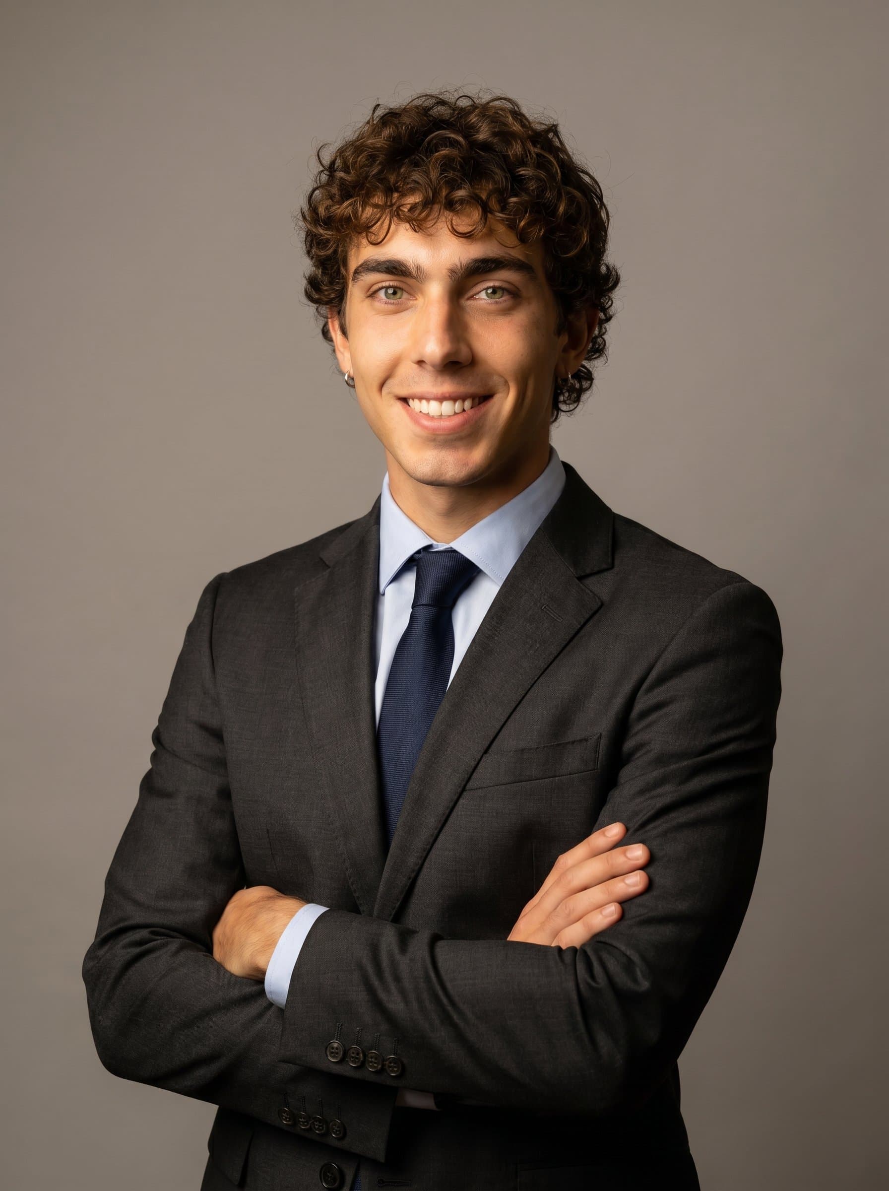 posed with arms crossed, formal suit, neutral backdrop, slight warm tone to enhance welcoming leadership qualities for a healthcare administration role.
