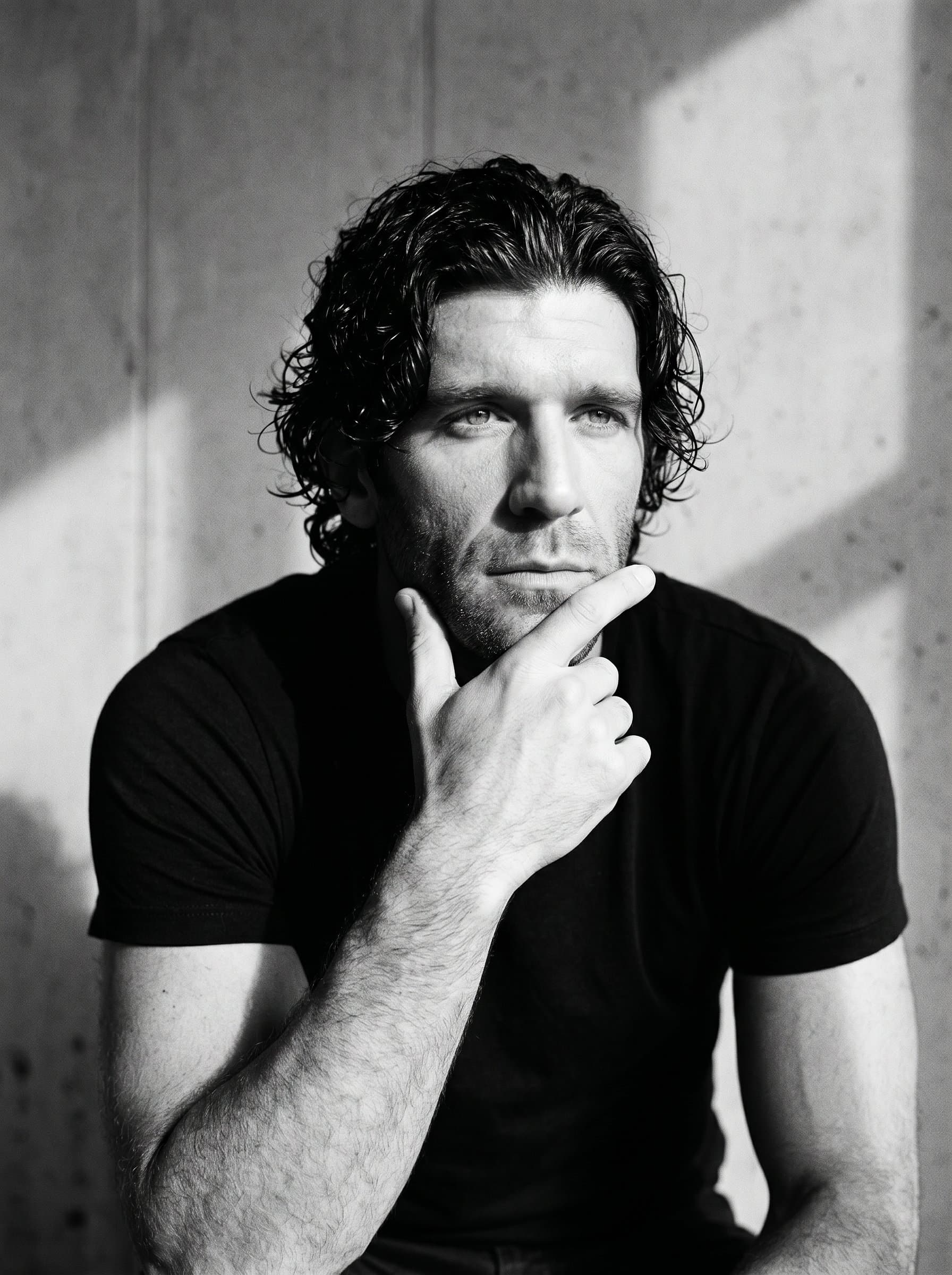 in a minimalist, monochrome studio setting, focusing on form and shadow. The man's pose and expression are contemplative, allowing their features to stand out against the stark simplicity of the background.