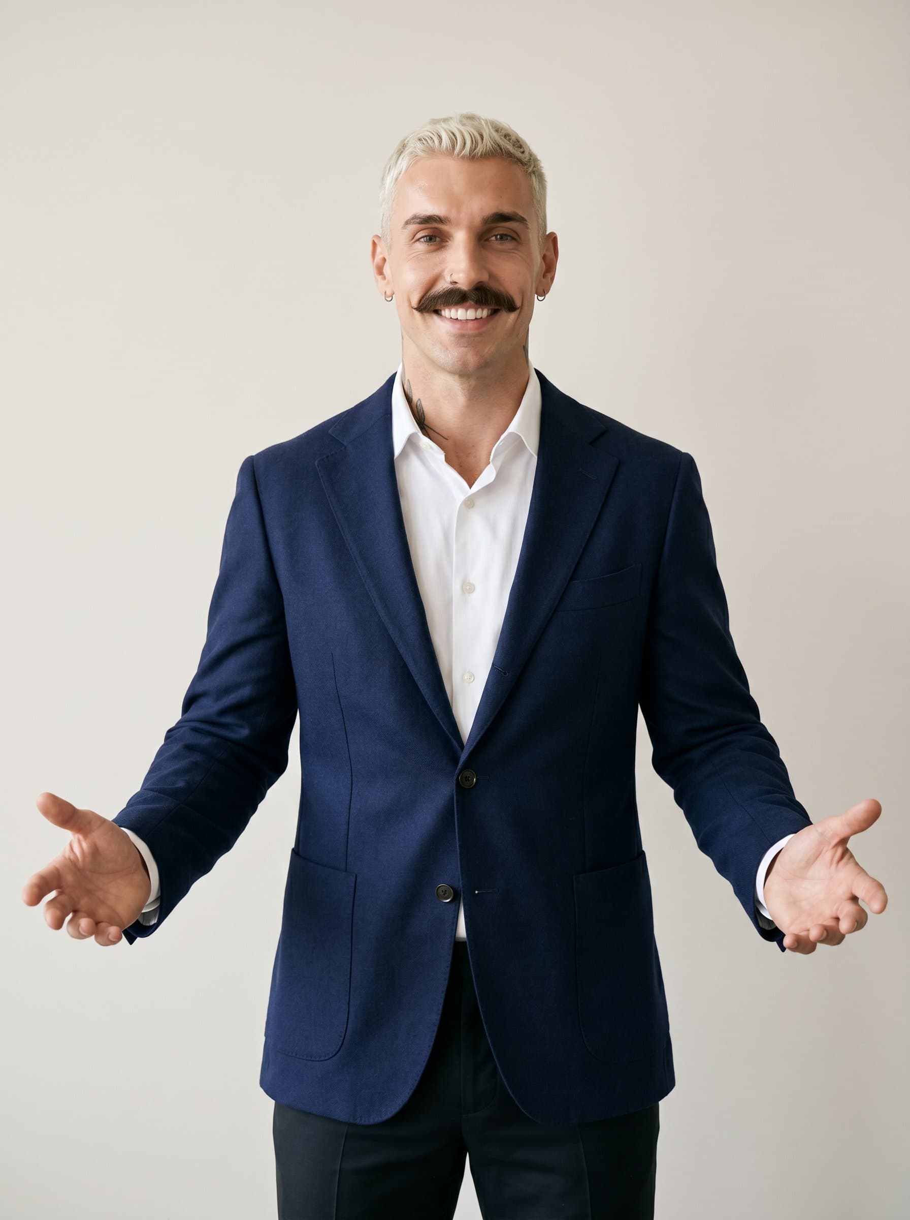 in a tailored jacket, slightly smiling with arms open wide. A neutral background accentuates their welcoming and inclusive aura, ideal for real estate open house invitations.