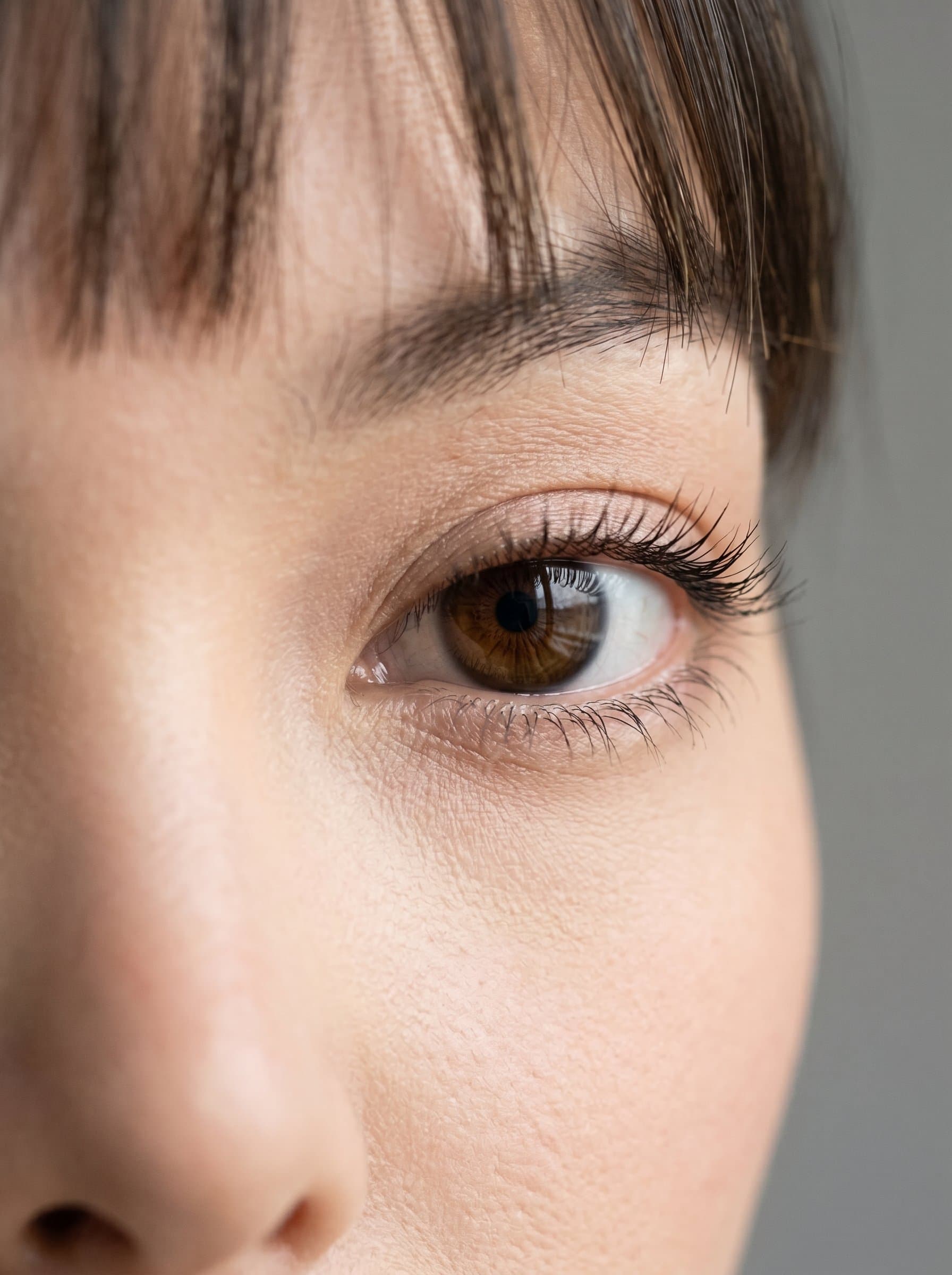 : Emphasize the model's eyes with a close-up shot, focusing on the depth and color, in a soft natural light setting, complemented by a simple grey backdrop.