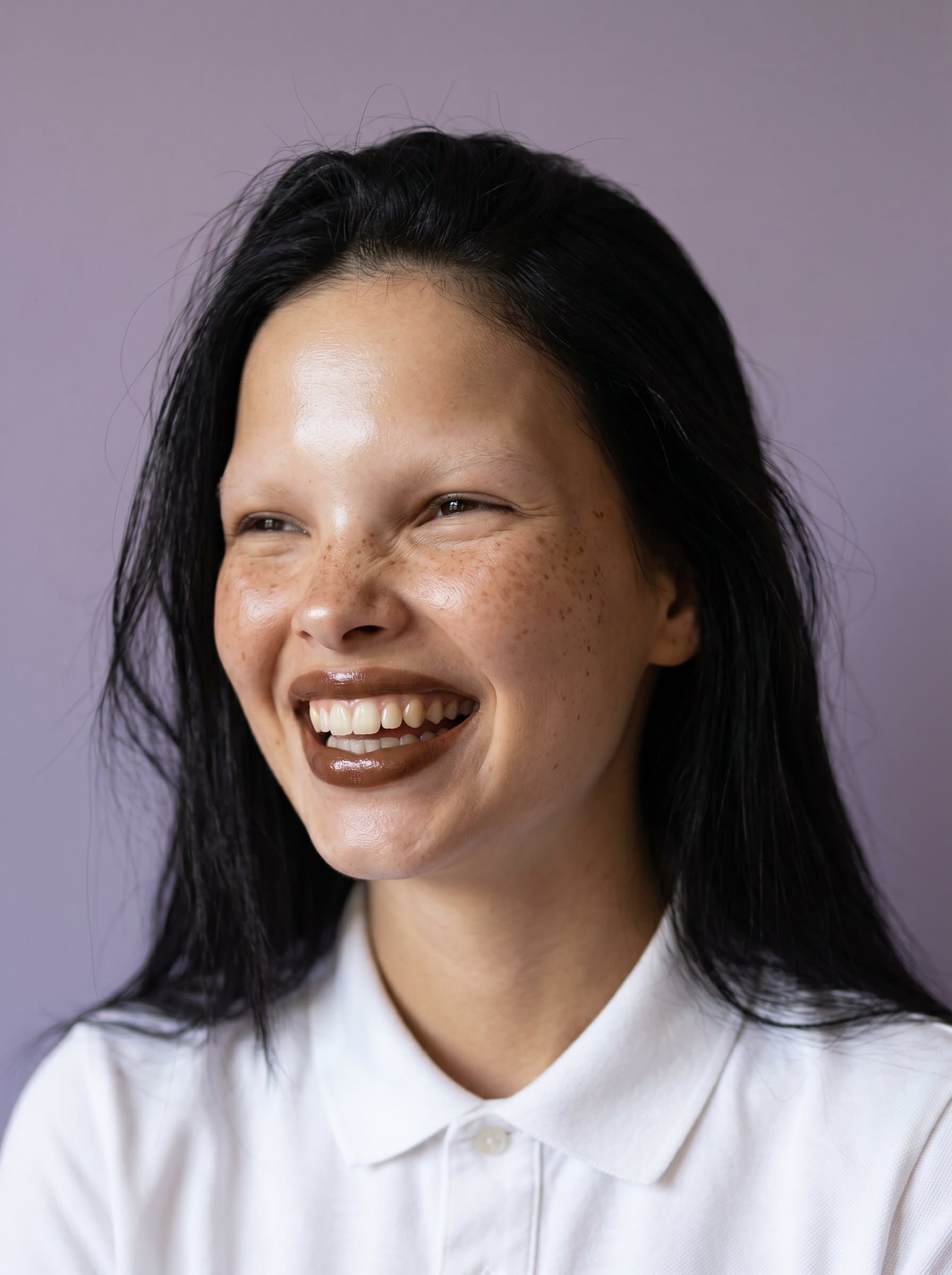 : Create a dynamic image with a candid laugh, focusing on natural expressions and luminous skin, set against a muted lavender backdrop to subtly enhance the model's features.