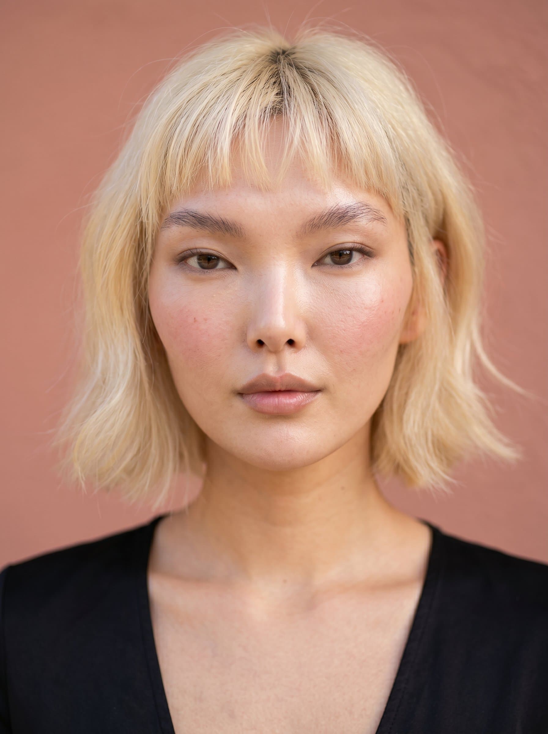 : Illustrate serene simplicity with a clean, radiant look, using natural light to highlight facial harmony, against a muted salmon background for a gentle yet striking image.