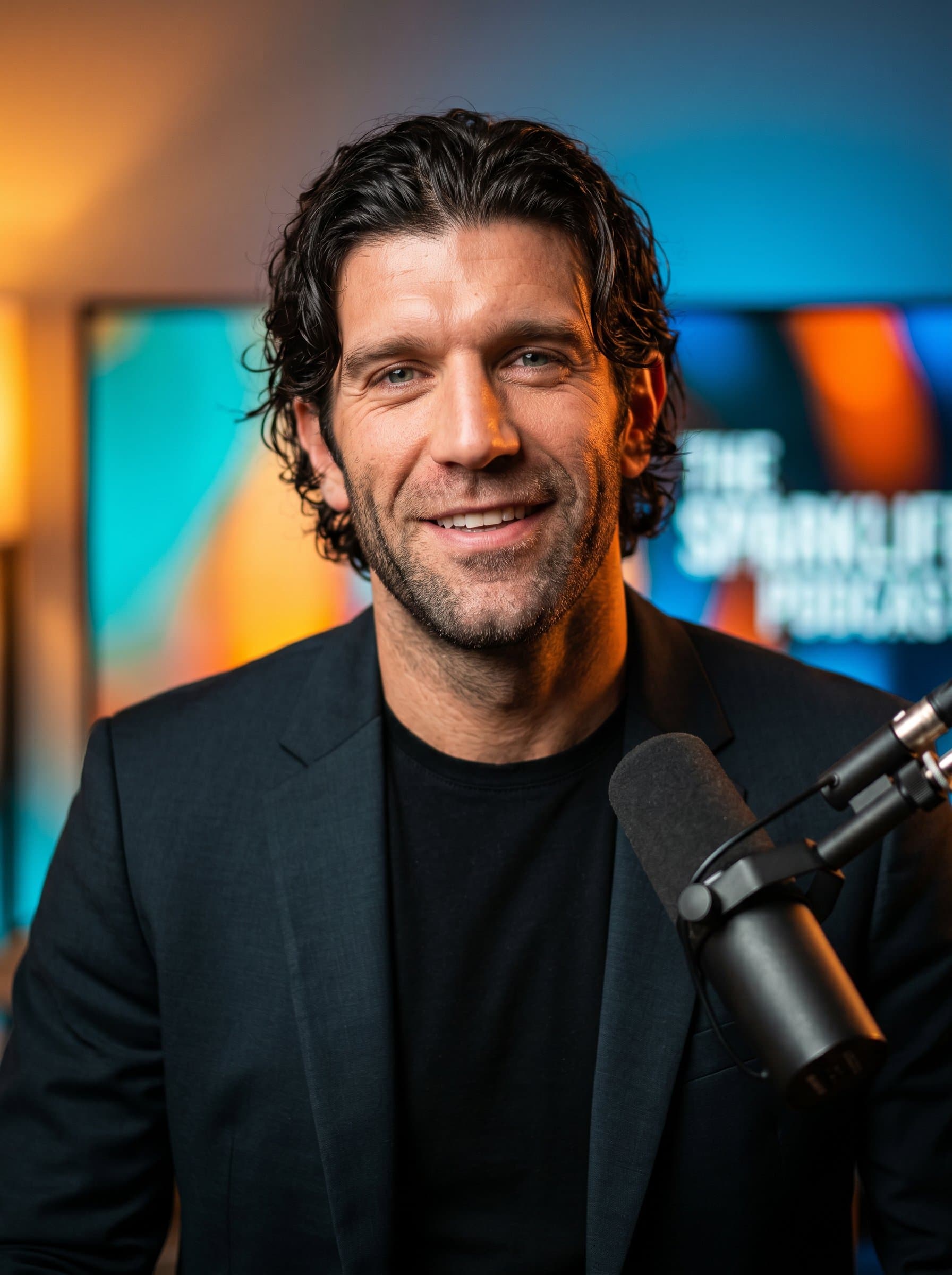 Warm headshot of a motivational podcast host, with a creative mix of vivid shades in the background, highlighting the man’s charismatic and dynamic personality in a photorealistic style.