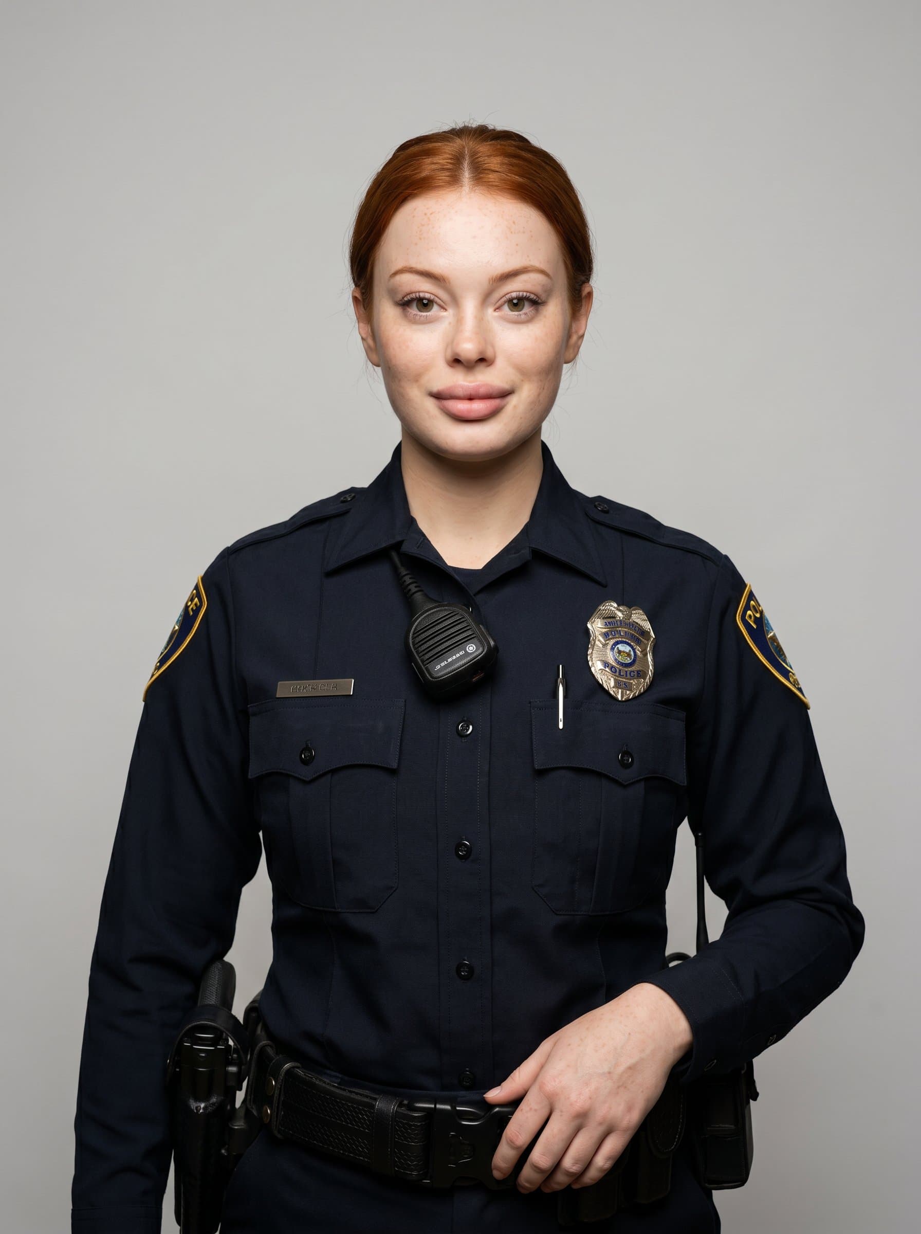 : Capture a police officer in full uniform with a calm expression, standing against a neutral gray background, illuminated by soft studio lighting to enhance facial features, conveying trust and professionalism.