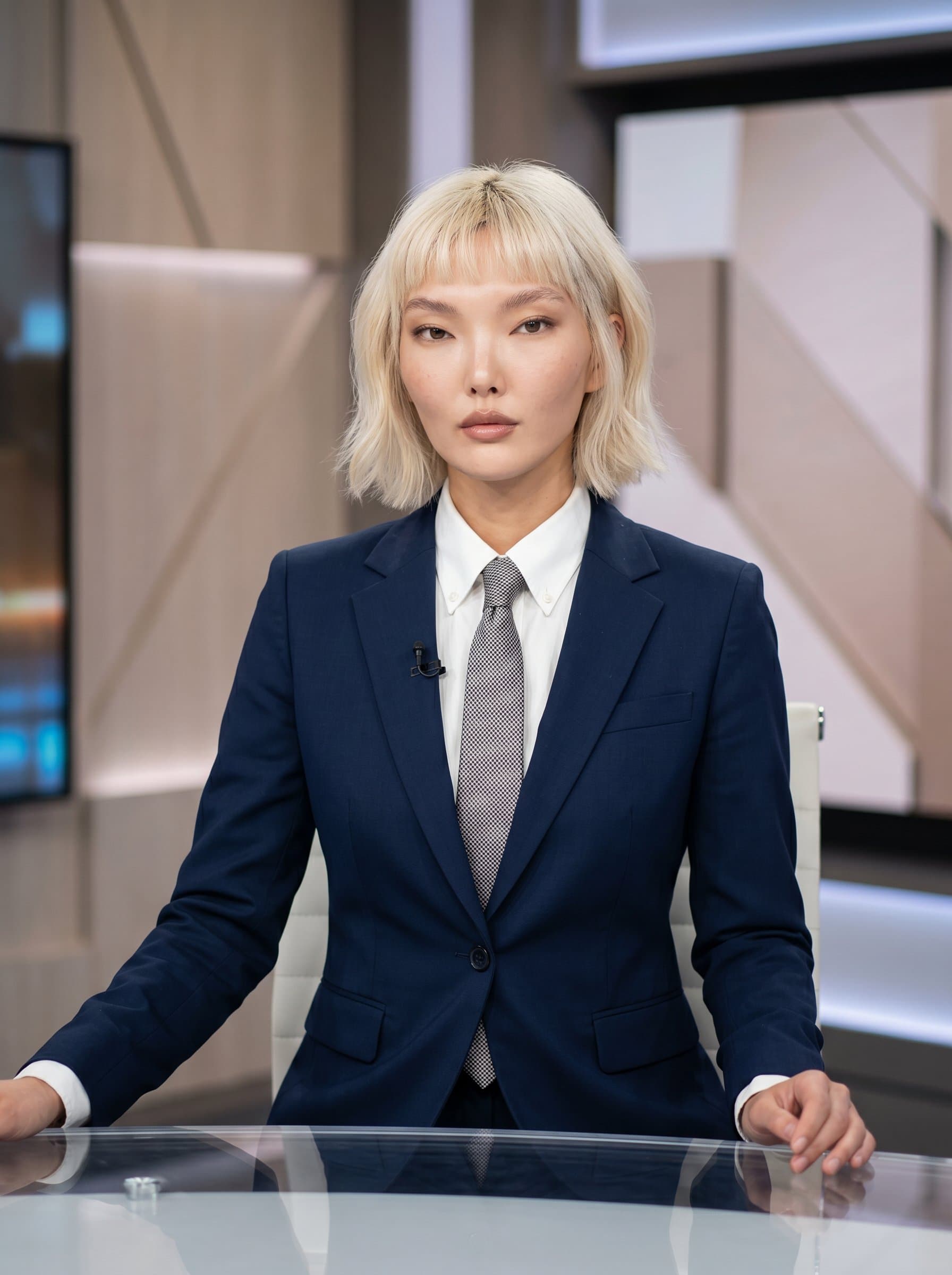 Professional portrait of exuding confidence in a suit. A neutral backdrop complements the subtle lighting that highlights their facial features for an ideal news anchor appearance.