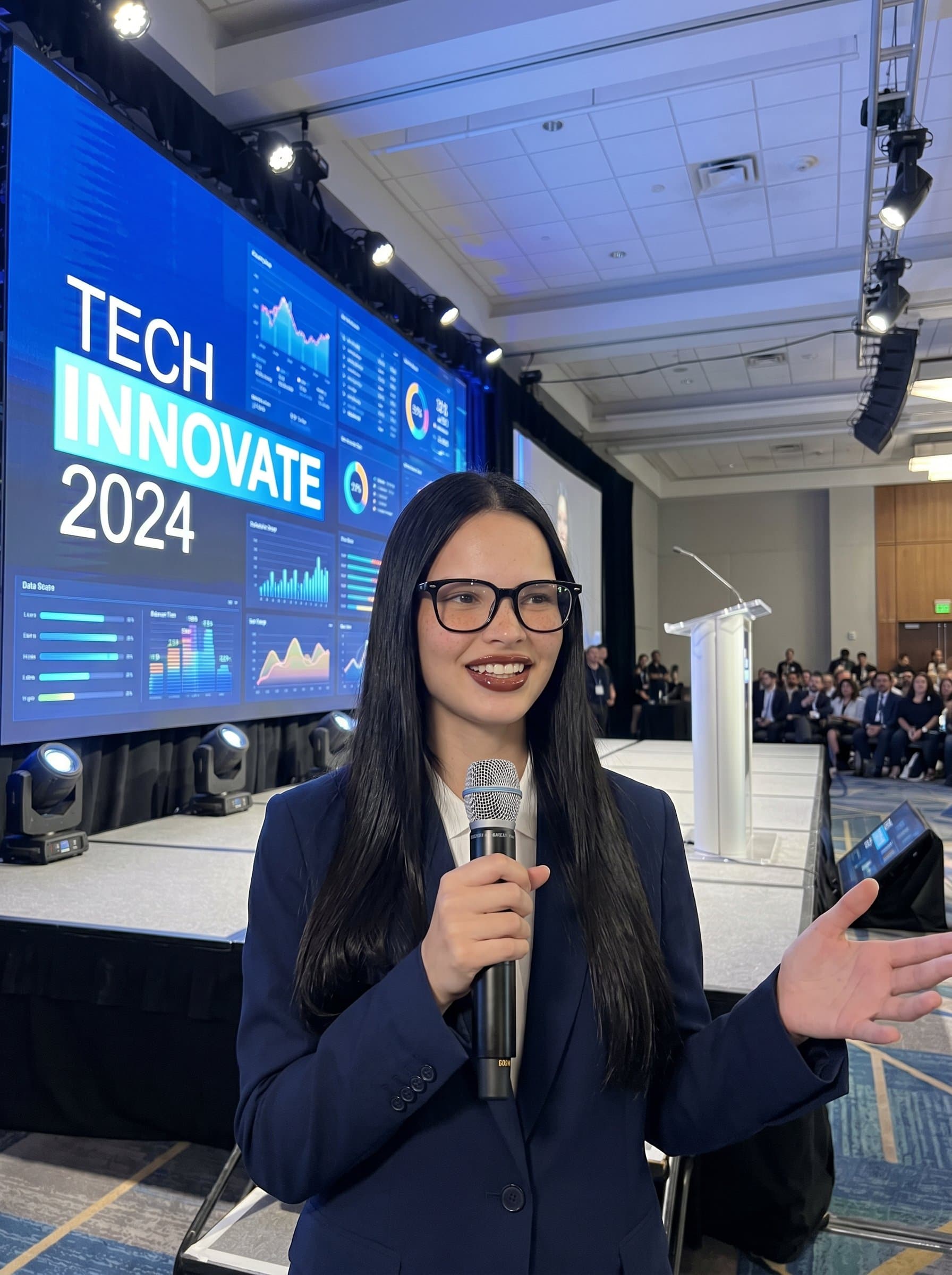 Create a of a keynote speaker at a tech conference, wearing a smart blazer and glasses, standing before a large digital screen displaying data visualizations.
