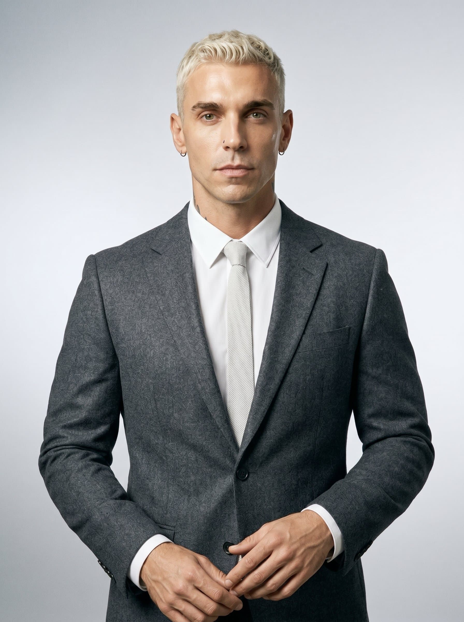 Render a portrait of a speaker with a focused expression, clean-shaven, and donning a modern-fit gray blazer. The minimalistic background, a soft silver gradient, emphasizes the speaker's calm and collected nature.