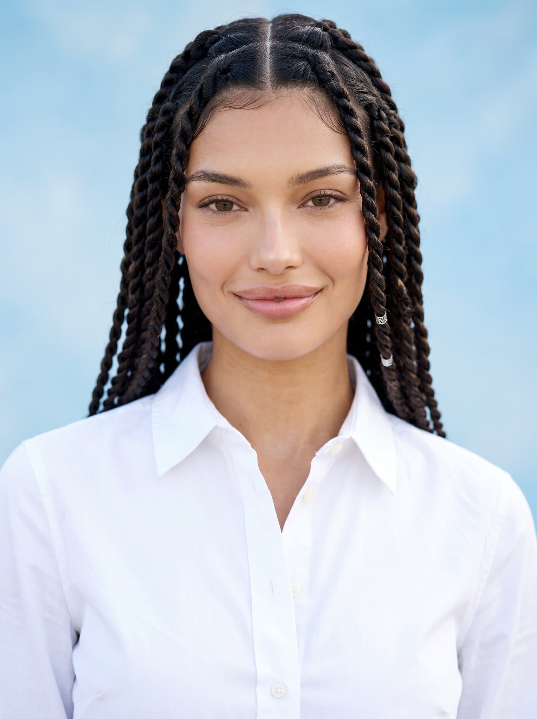 Design a headshot displaying a speaker with a composed demeanor, styled hair, and a classic white shirt. The airy blue background enhances the woman's serene smile and professional poise.