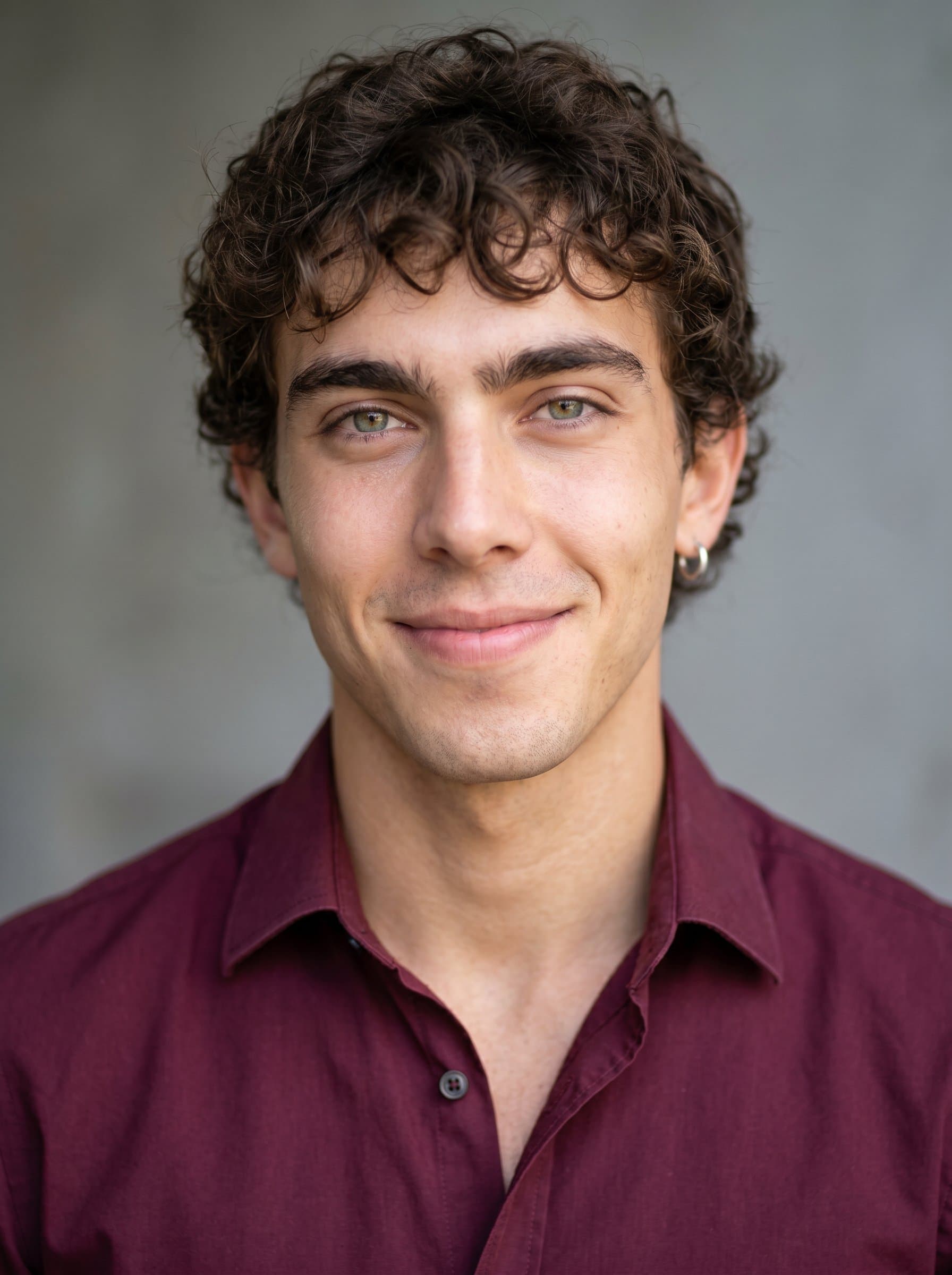 Fashion a headshot featuring a speaker with a gentle smile, dressed in a maroon dress shirt. The soft gray backdrop enhances the speaker's professional image and clear, welcoming complexion.