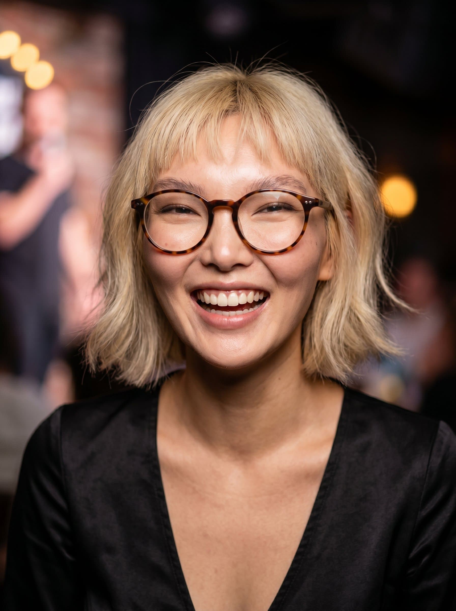: Close-up of a comedian with an infectious smile, sporting trendy glasses. The background fades out to emphasize their charismatic expression, ideal for social media promotion.