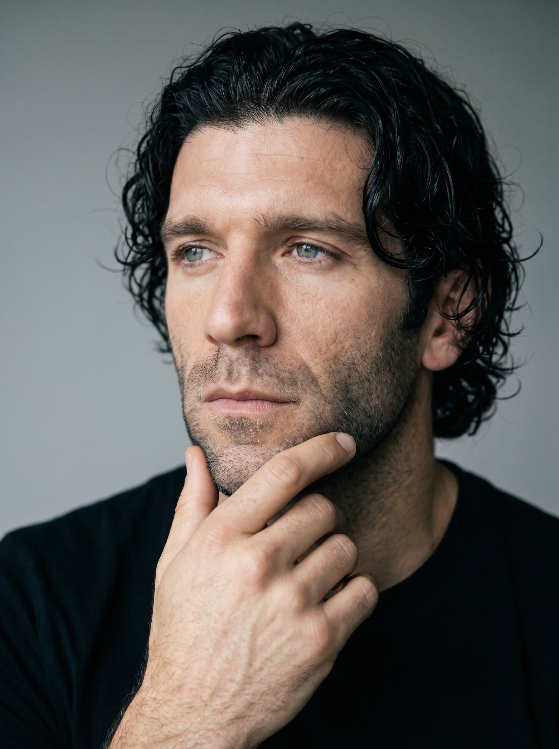: Headshot of a comedian in an introspective moment, gaze directed off-camera. The soft lighting and simple backdrop emphasize their thoughtful side, capturing depth and humor.