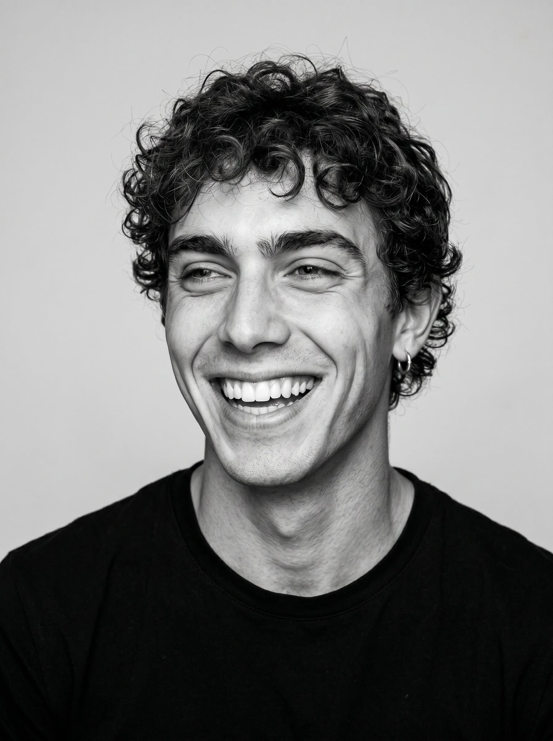 : A minimalist black-and-white headshot of a comedian, capturing a moment of genuine amusement. Their simplicity and authenticity are forefront against a plain backdrop.