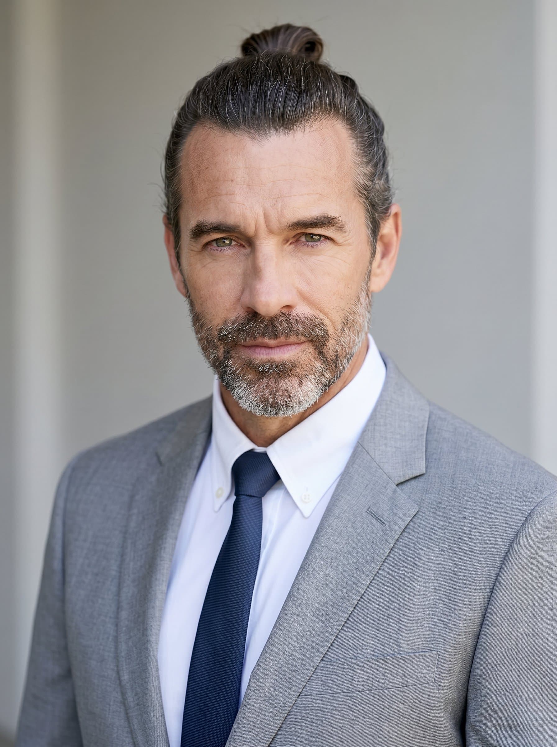 : Professional headshot of a data scientist with a bun, in a light grey suit. The neutral background and soft lighting highlight the man's thoughtful gaze and composed expression.