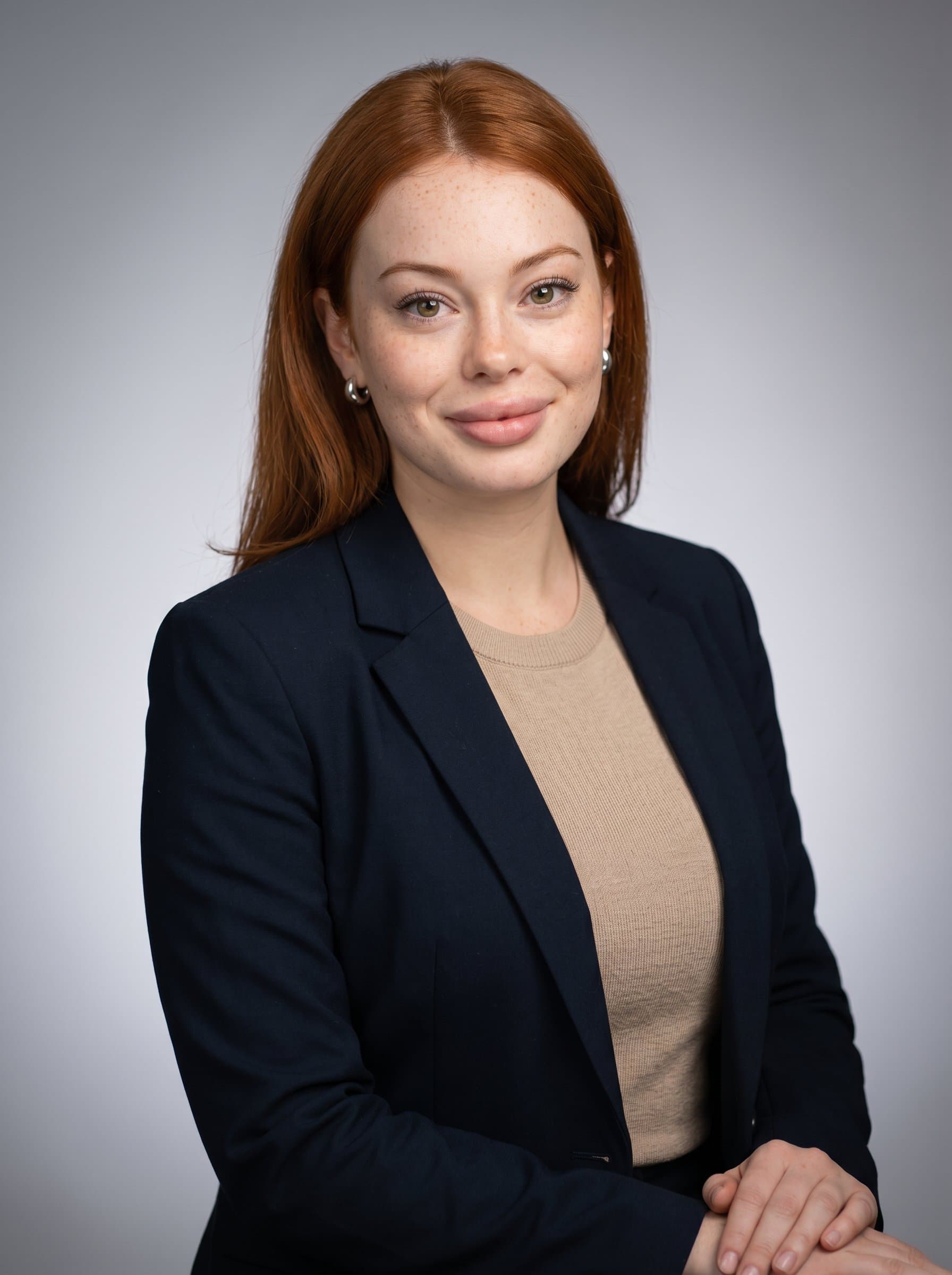 Capture a HR professional smiling softly against a gradient grey background, dressed in business-casual attire. The lighting accentuates their features, portraying them as inclusive and approachable, ready for a leadership role.