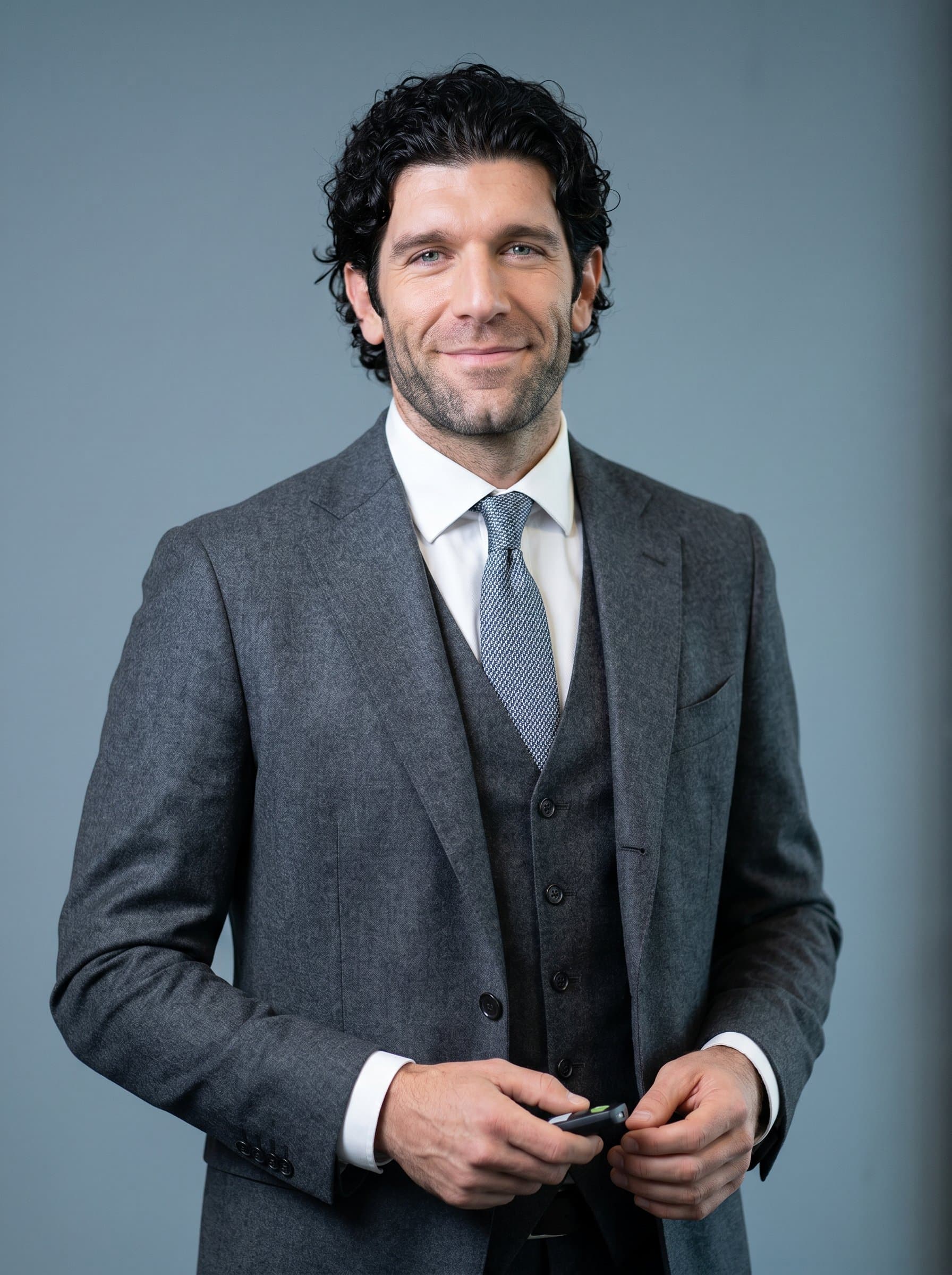 Show a HR manager in a white-collar environment, with a neutral blue-grey background. The conservative yet stylish attire and empathetic smile project reliability and openness, suitable for corporate presentations.