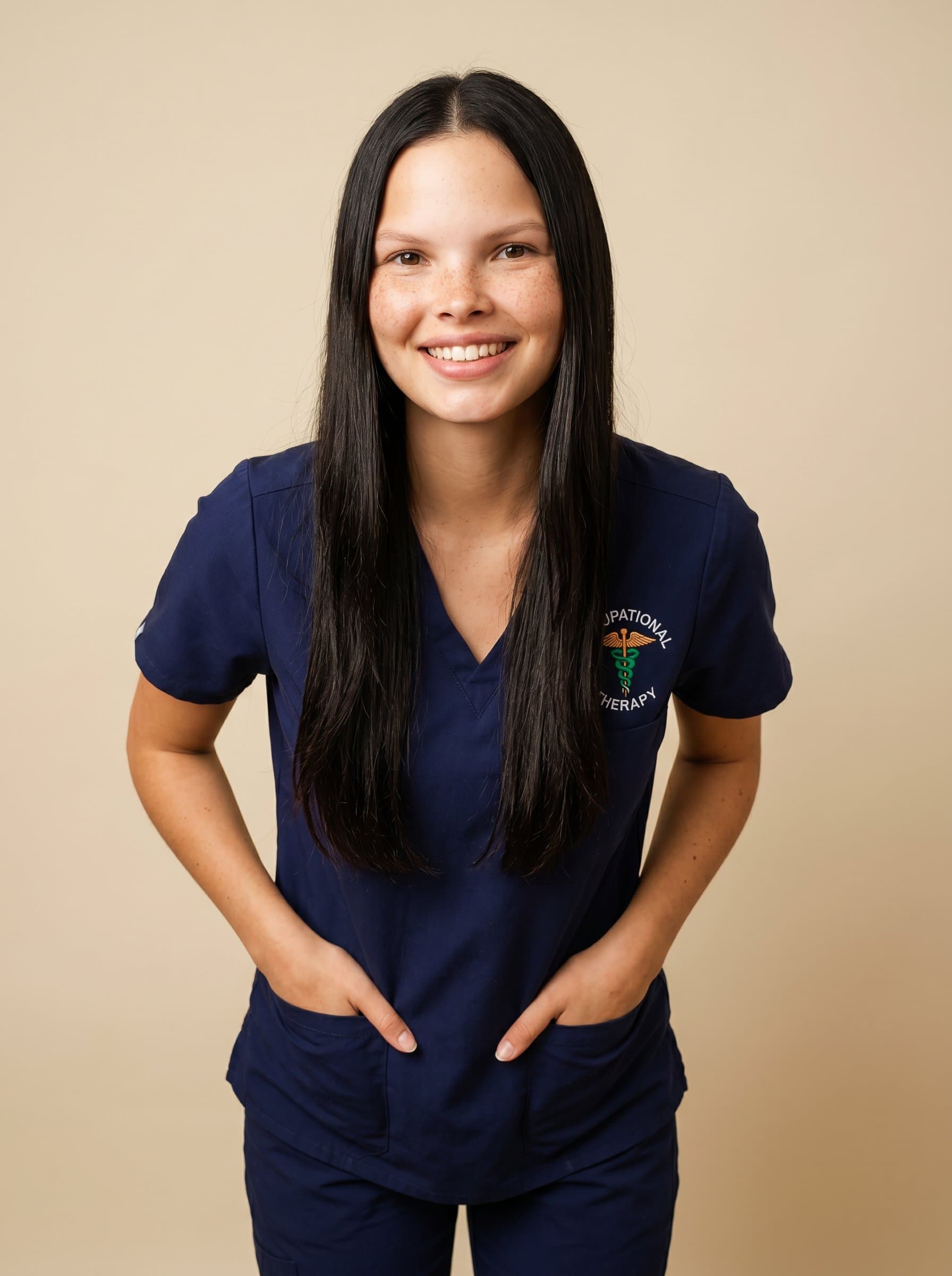 A occupational therapist leaning slightly forward, hands in pockets, with an inviting smile. The neutral cream background enhances their friendly, yet authoritative presence.