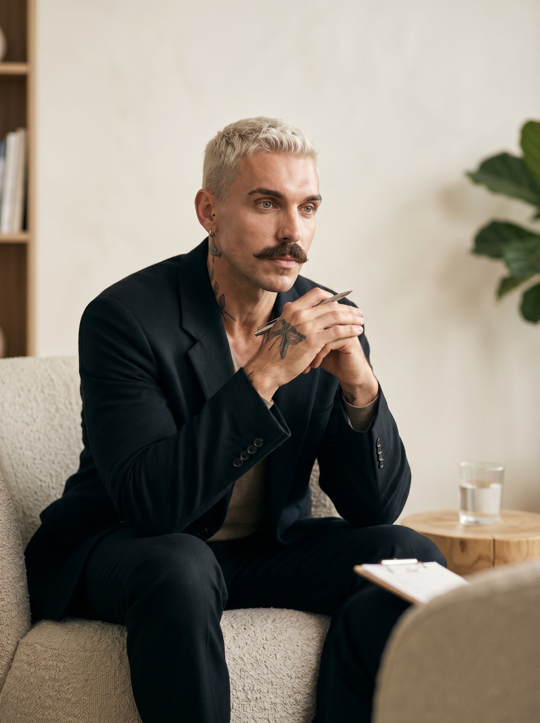 A therapist, with a slight tilt of the head and a thoughtful gaze. The neutral ivory background enhances their contemplative and understanding demeanor.