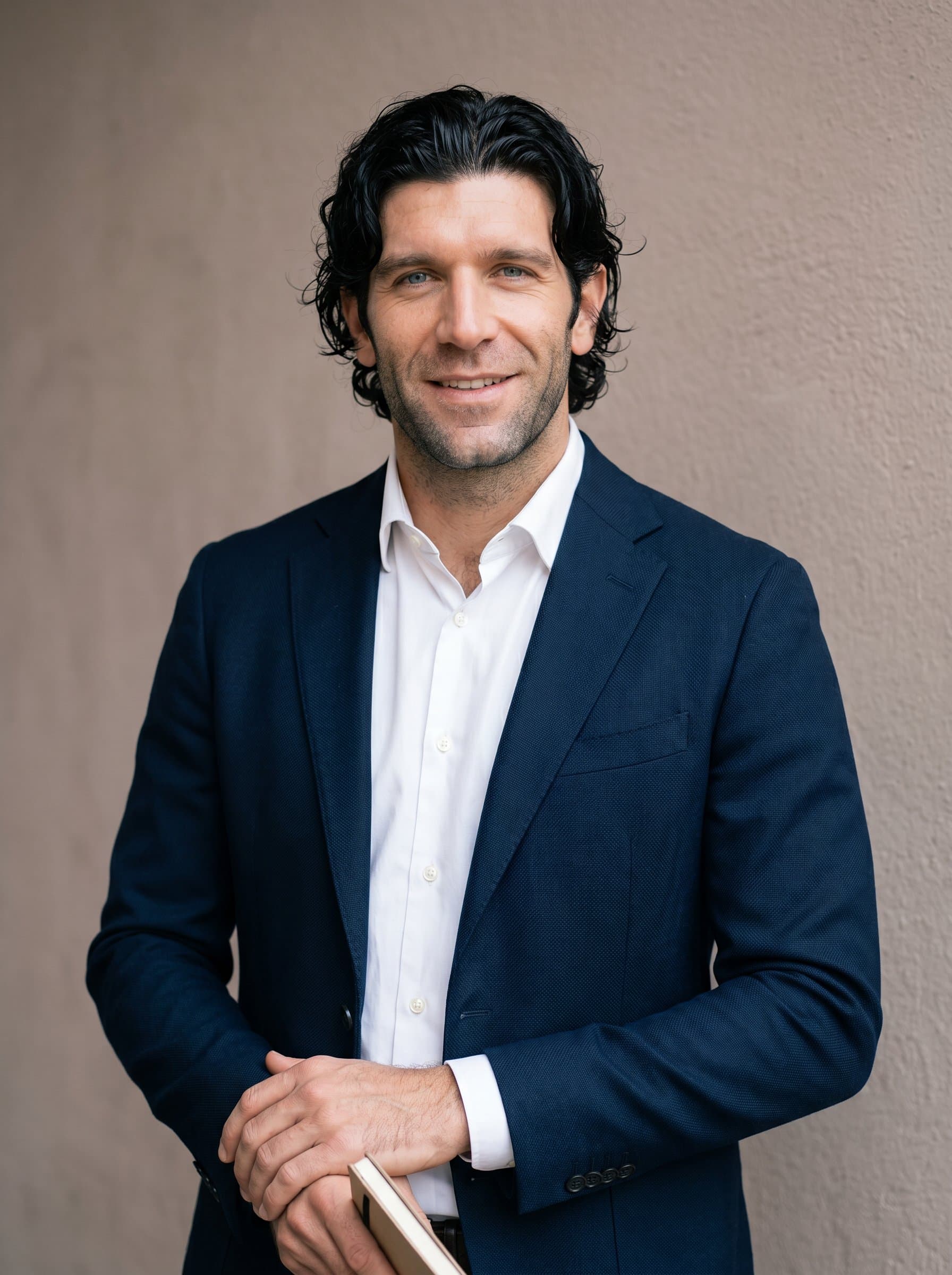 With an attentive expression, poses against a soft, taupe wall. Their neat blazer and poised demeanor project an image of reliability and leadership within the educational community.