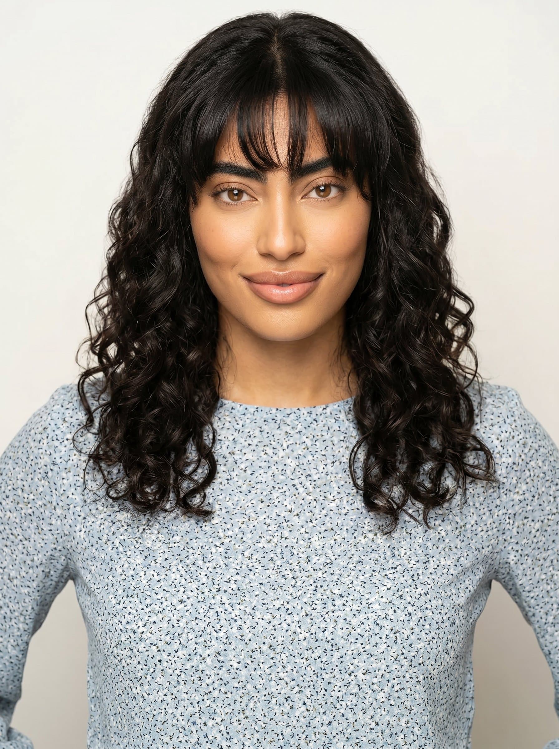 in a subtle patterned blouse, stands before a simple, off-white backdrop. Their confident yet gentle smile communicates openness and readiness to engage with colleagues and the school community.
