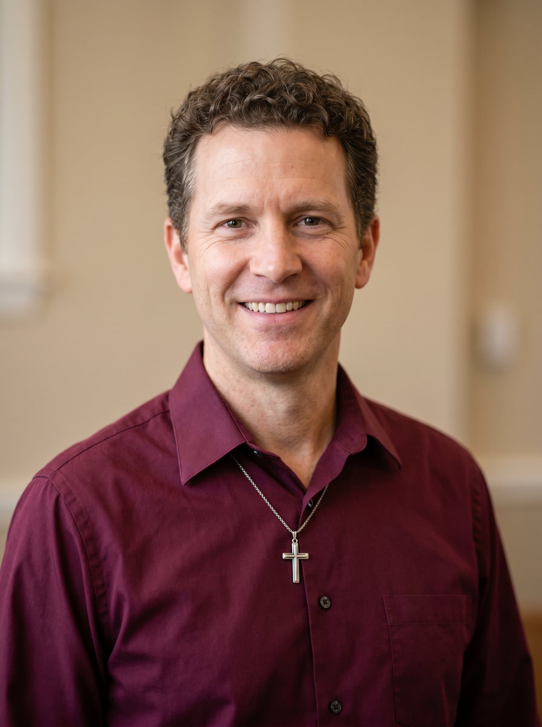 : Generate a pastor's headshot showcasing a trusting and sincere demeanor, in a neatly pressed burgundy shirt, with a soft beige background that highlights their compassionate role in the community.