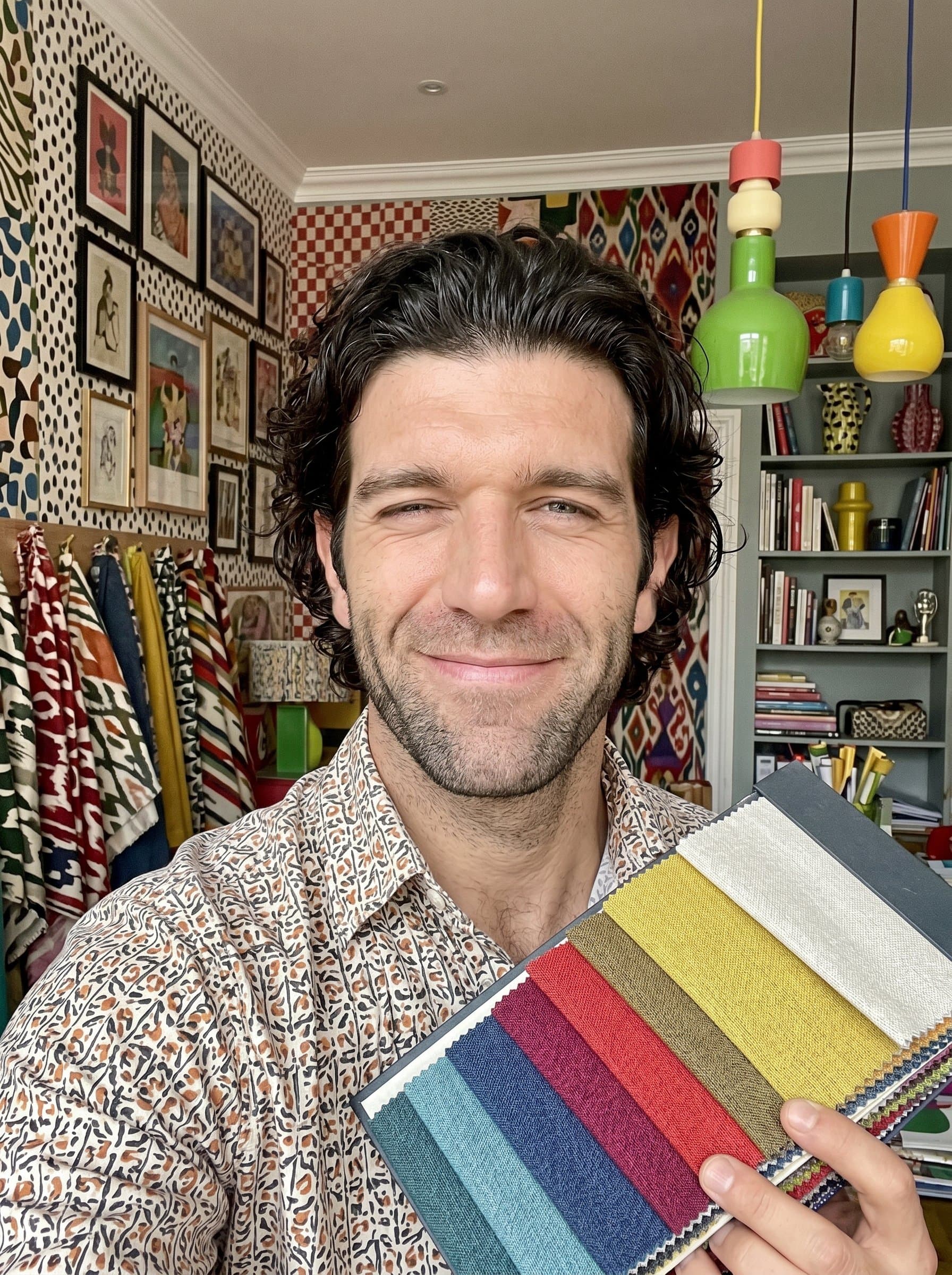 A headshot featuring an interior designer, against a colorful, eclectic backdrop. The image should showcase the man's playful personality and adventurous approach to mixing different design styles.
