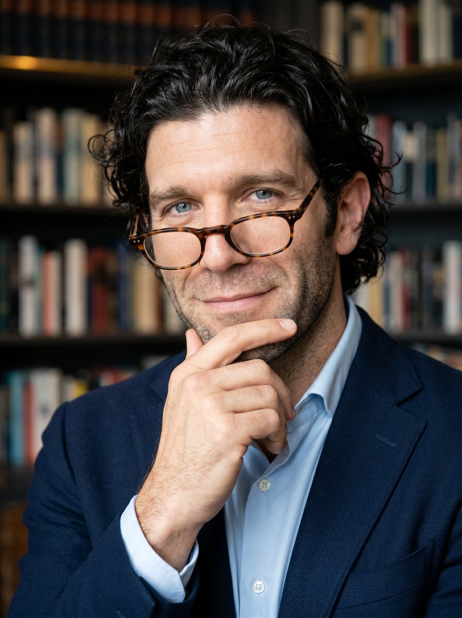 in a business casual setting with glasses perched on their nose. The expression is thoughtful yet approachable. The background is a simple, elegant library, suggesting knowledge and professionalism.