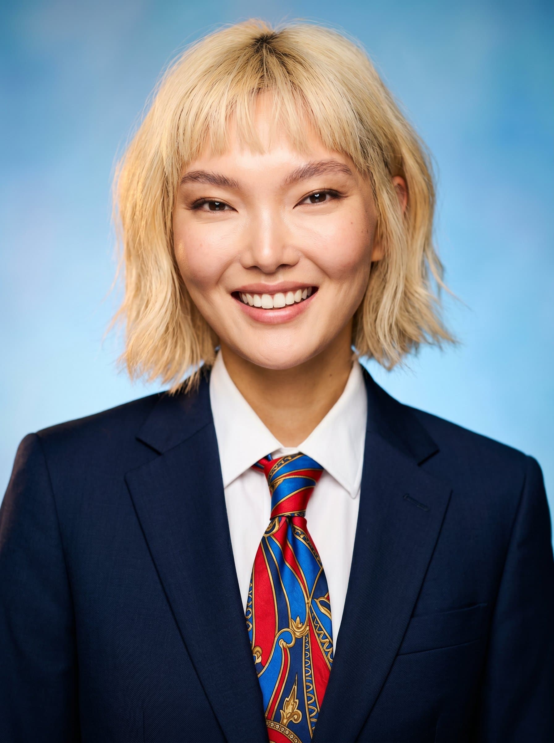 Vibrant featuring bold colors. The agent is wearing a dark suit with a striking tie. The background is a gradient of light blues, focusing attention on the agent’s welcoming smile.