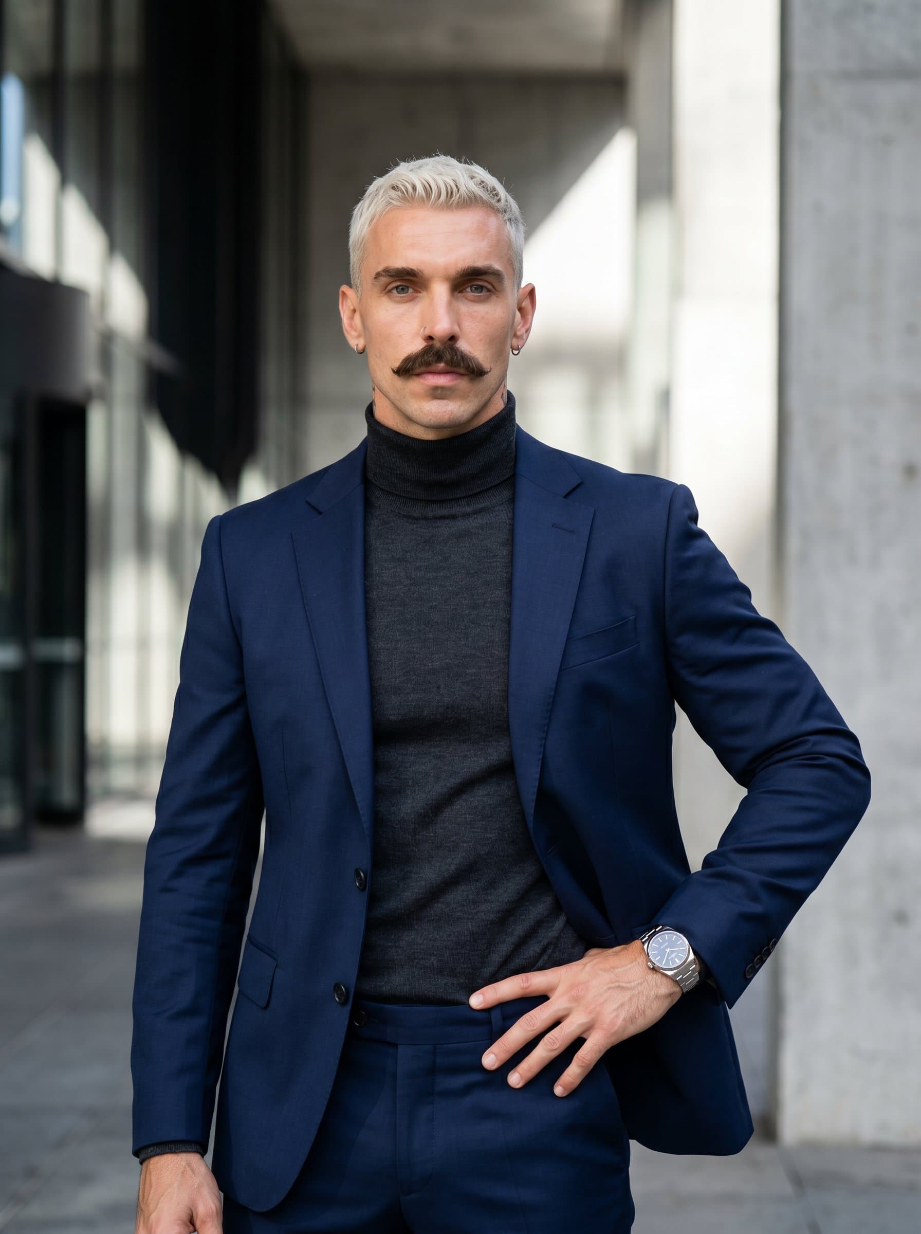 Sophisticated featuring the agent in a designer suit, set against a backdrop of subtle, modern architecture. The expression is poised and confident, suggesting a forward-thinking professional approach.