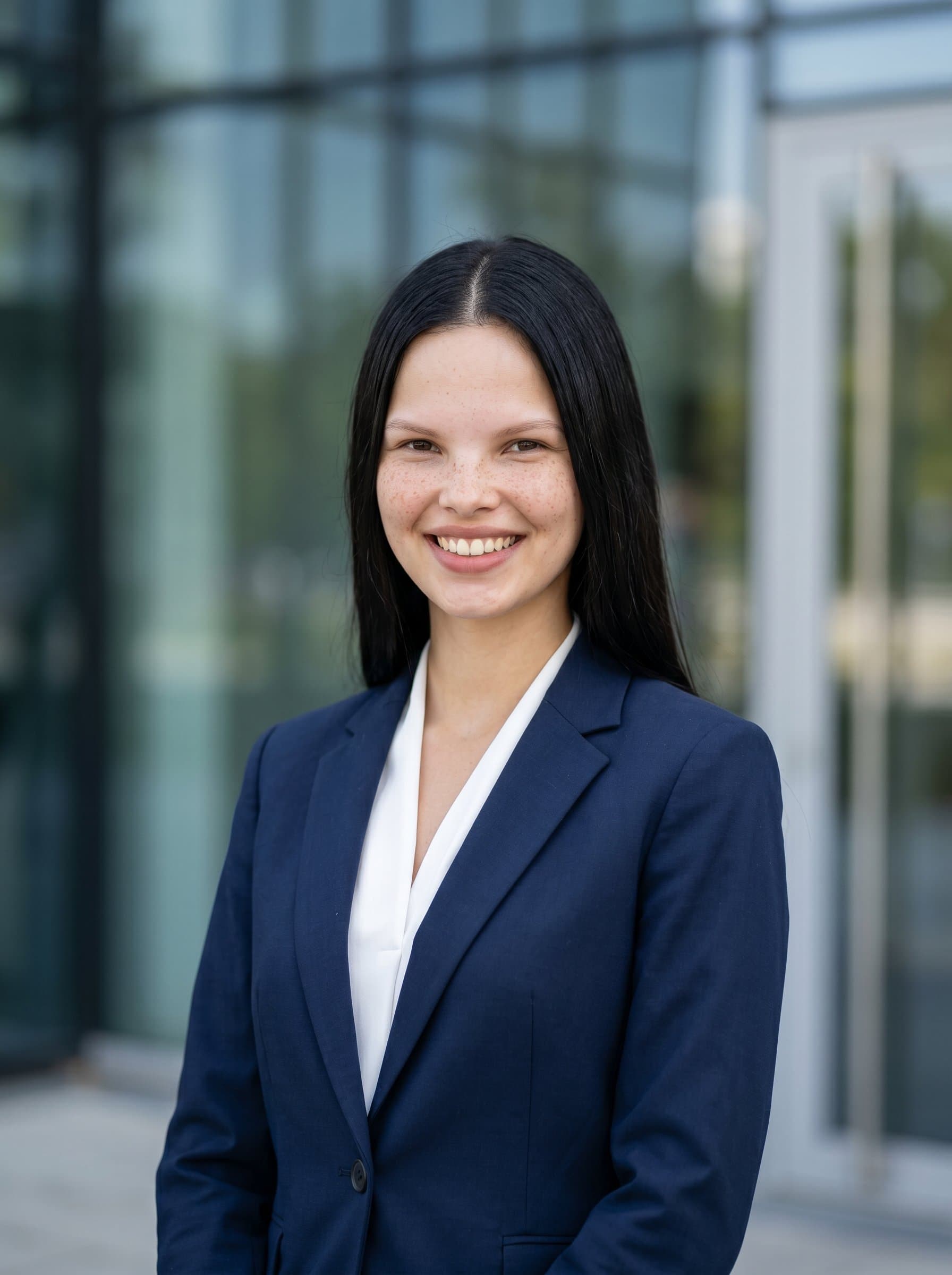 Create a headshot of a mortgage broker in a classic style, wearing a tailored suit, standing confidently in front of a sleek office building, with a warm, approachable smile that conveys trust and professionalism.