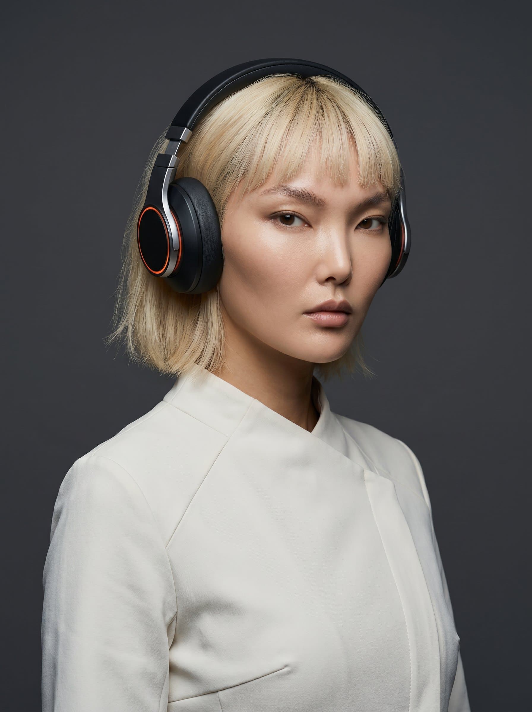 : Design a minimalist DJ headshot with a plain solid-color background, featuring sleek headphones and modern attire. Photorealistic, clean lines, subtle lighting.