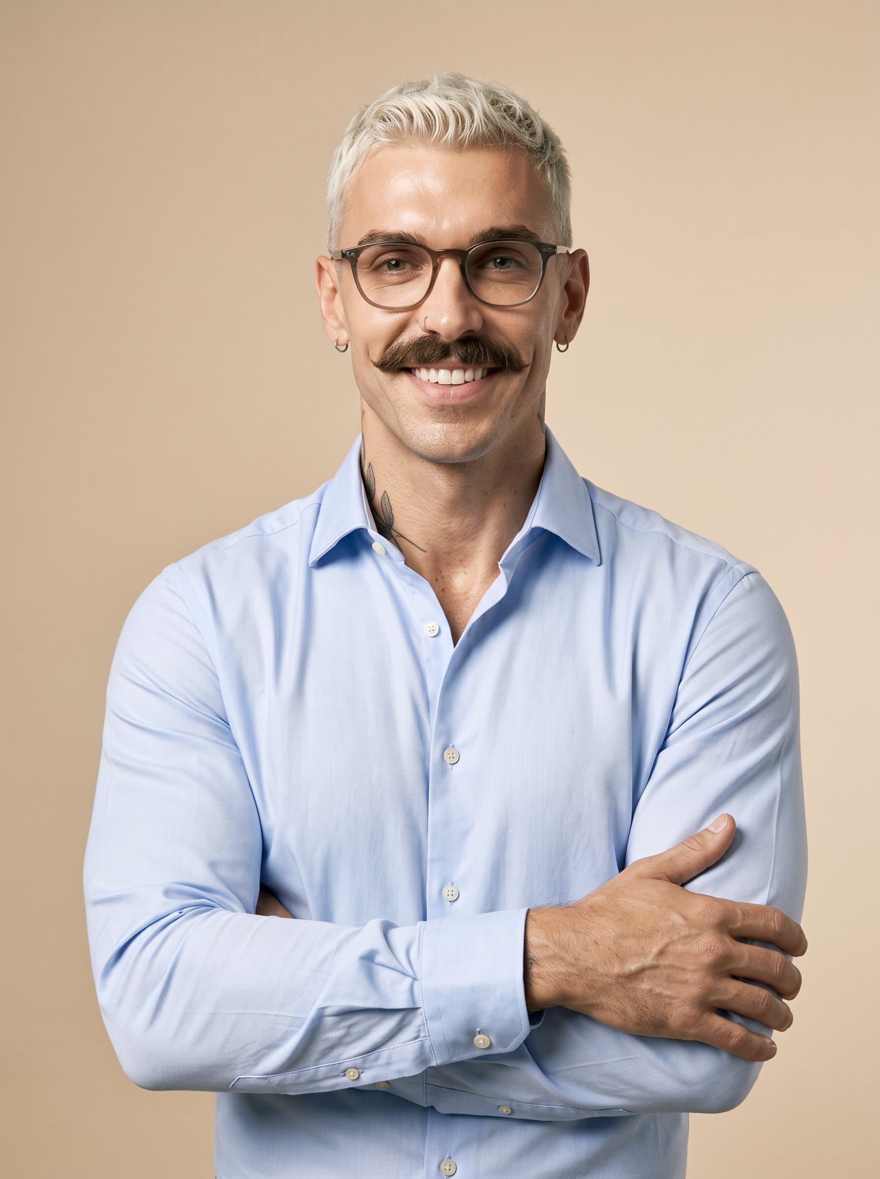 In a well-lit space, a poised man with glasses, dressed in a smart shirt, stands confidently with highlighting their warmth and professionalism against a simple beige backdrop.