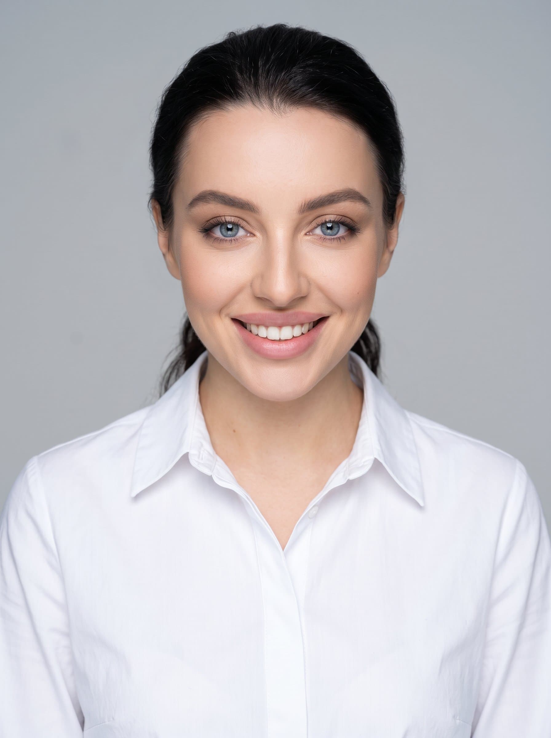 A polished media planner with long hair tied back, wearing a collared shirt. captures their welcoming smile against an understated gray background.