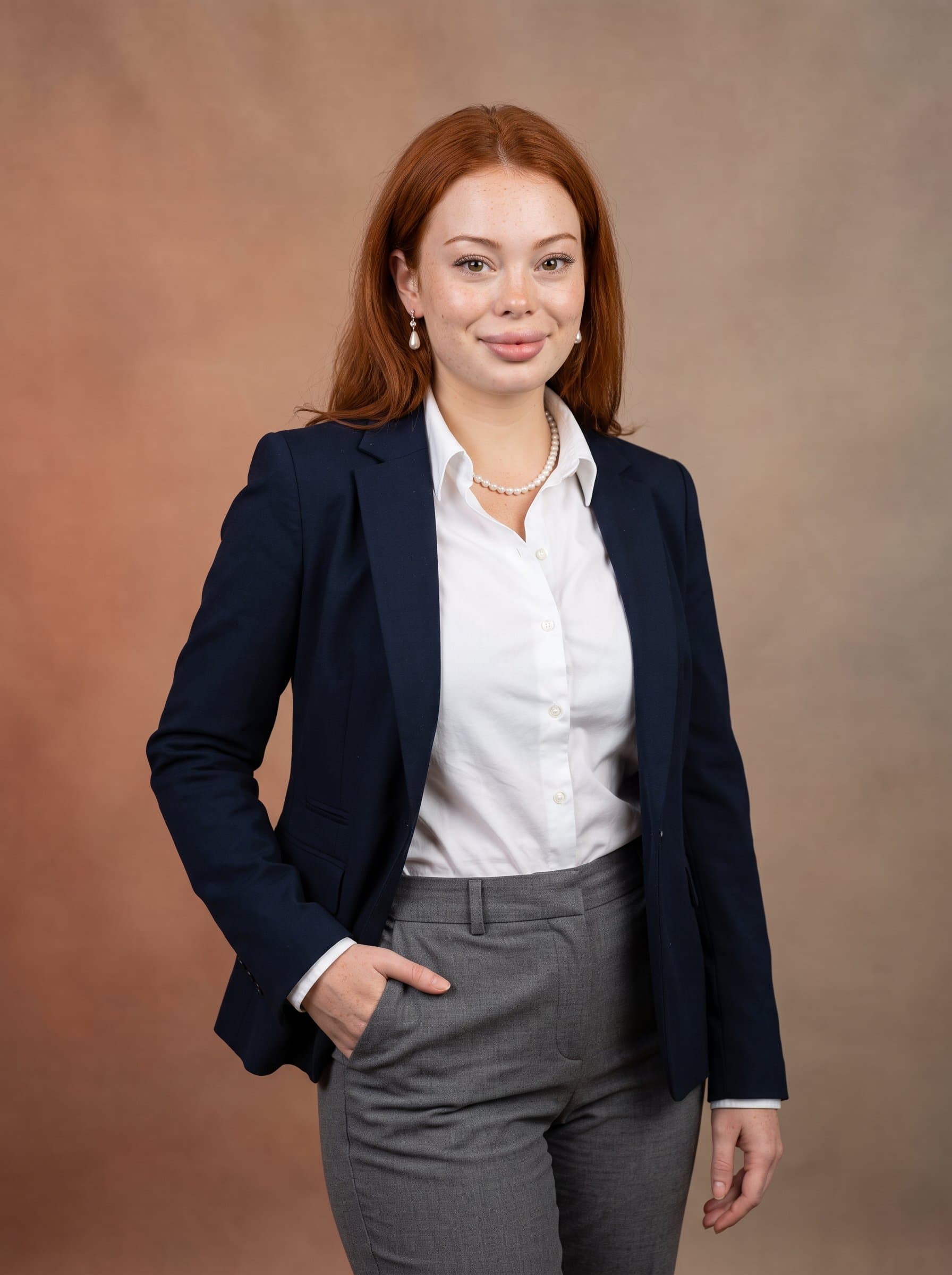 standing confidently with a soft smile, wearing a tailored blazer and a crisp shirt. The background is a subtle gradient of earth tones, emphasizing a professional demeanor yet approachable essence.