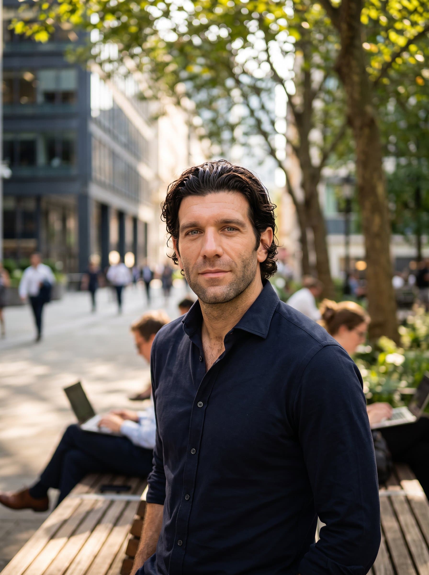 portrayed mid-shot, with a serene expression and an inviting gaze. The backdrop is a blurred urban park scene, suggesting a blend of nature and human-centered work ethic.