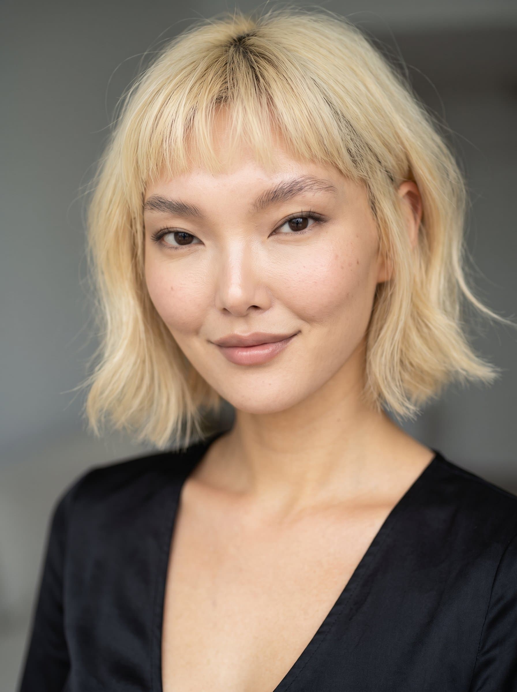 : Create a headshot featuring a subtle, knowing smile, with even lighting to accentuate the eyes, set against a soft gray background to convey warmth and approachability.