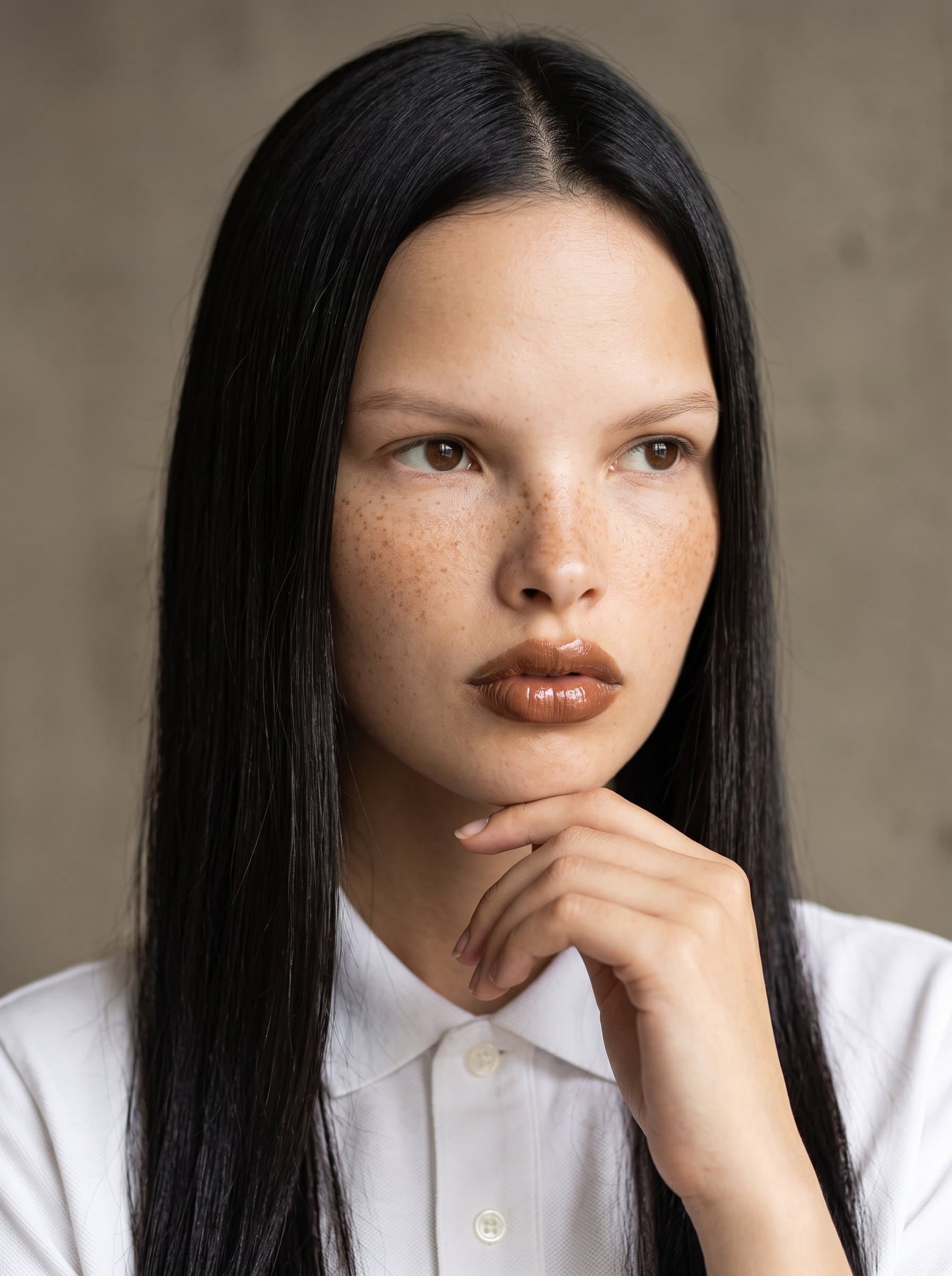 : Create a headshot with a pensive, slightly distant gaze, using balanced lighting to bring out facial features, set against a minimalist backdrop to convey depth and storytelling ability.