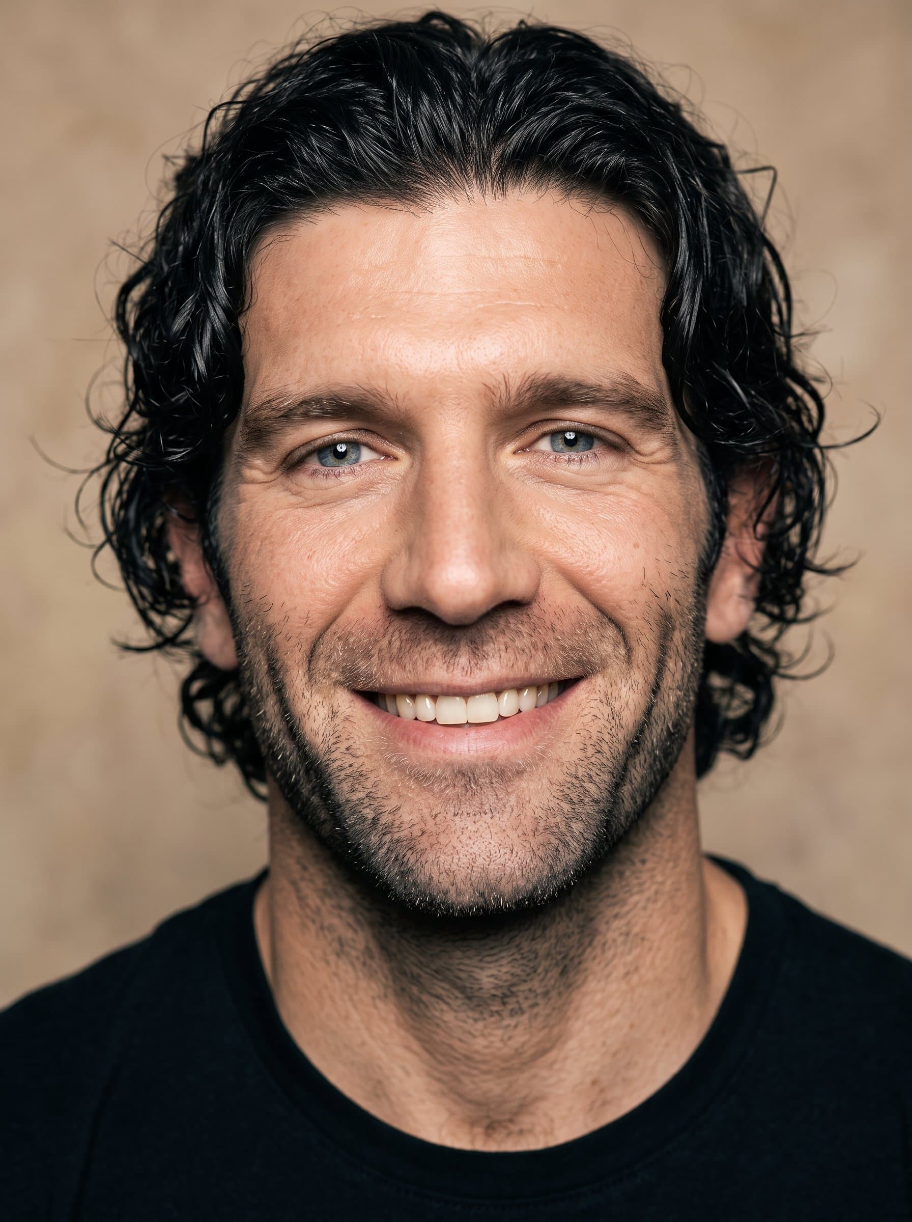 : Emphasize a genuine smile with careful lighting to highlight the eyes and cheekbones, surrounded by a soft beige background that enhances the actor's approachable and friendly demeanor.