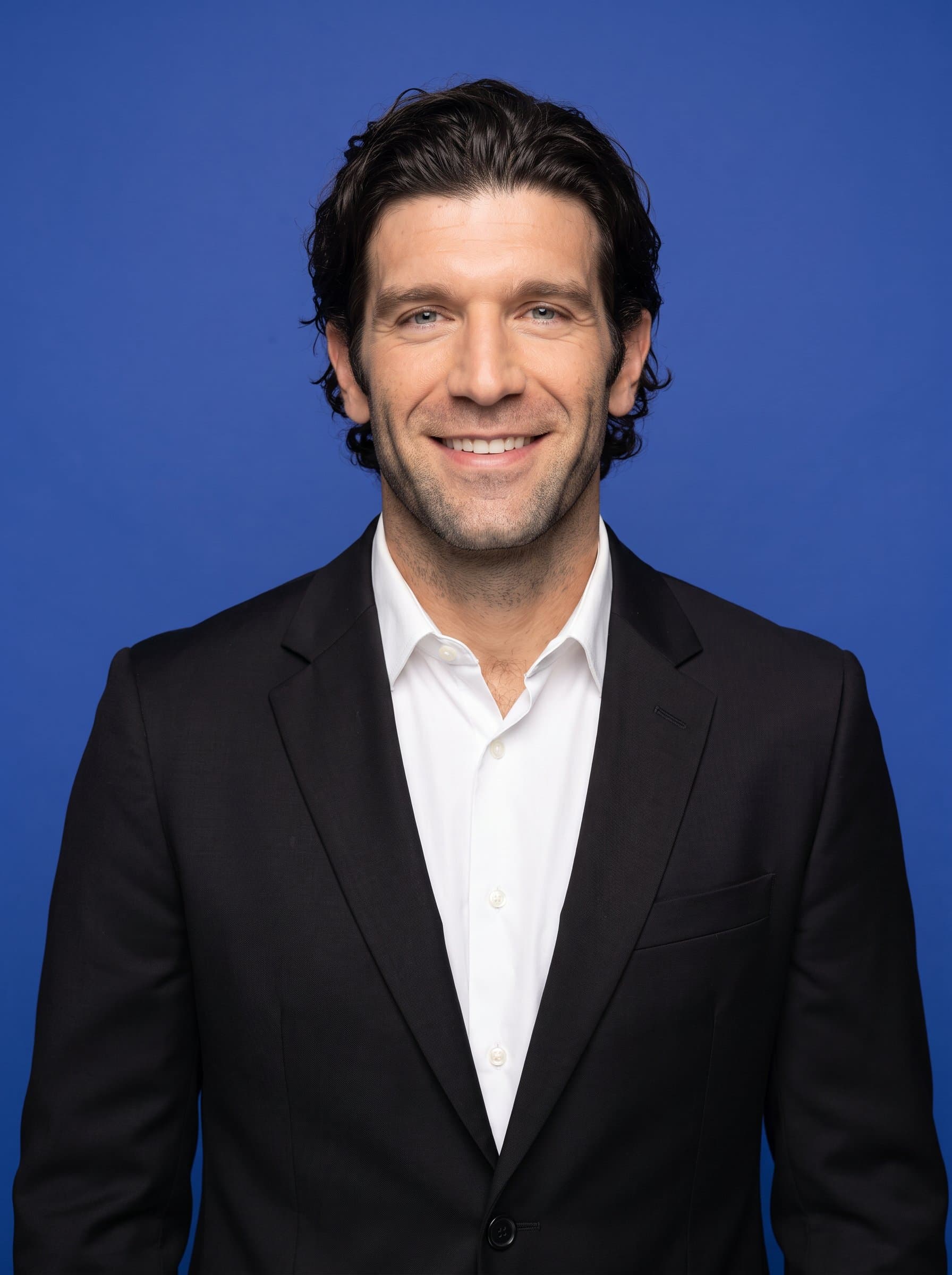 : Capture a government employee against a solid blue background, wearing a fitted black blazer, smiling warmly, symbolizing professionalism and approachability for official documentation. Photorealistic.