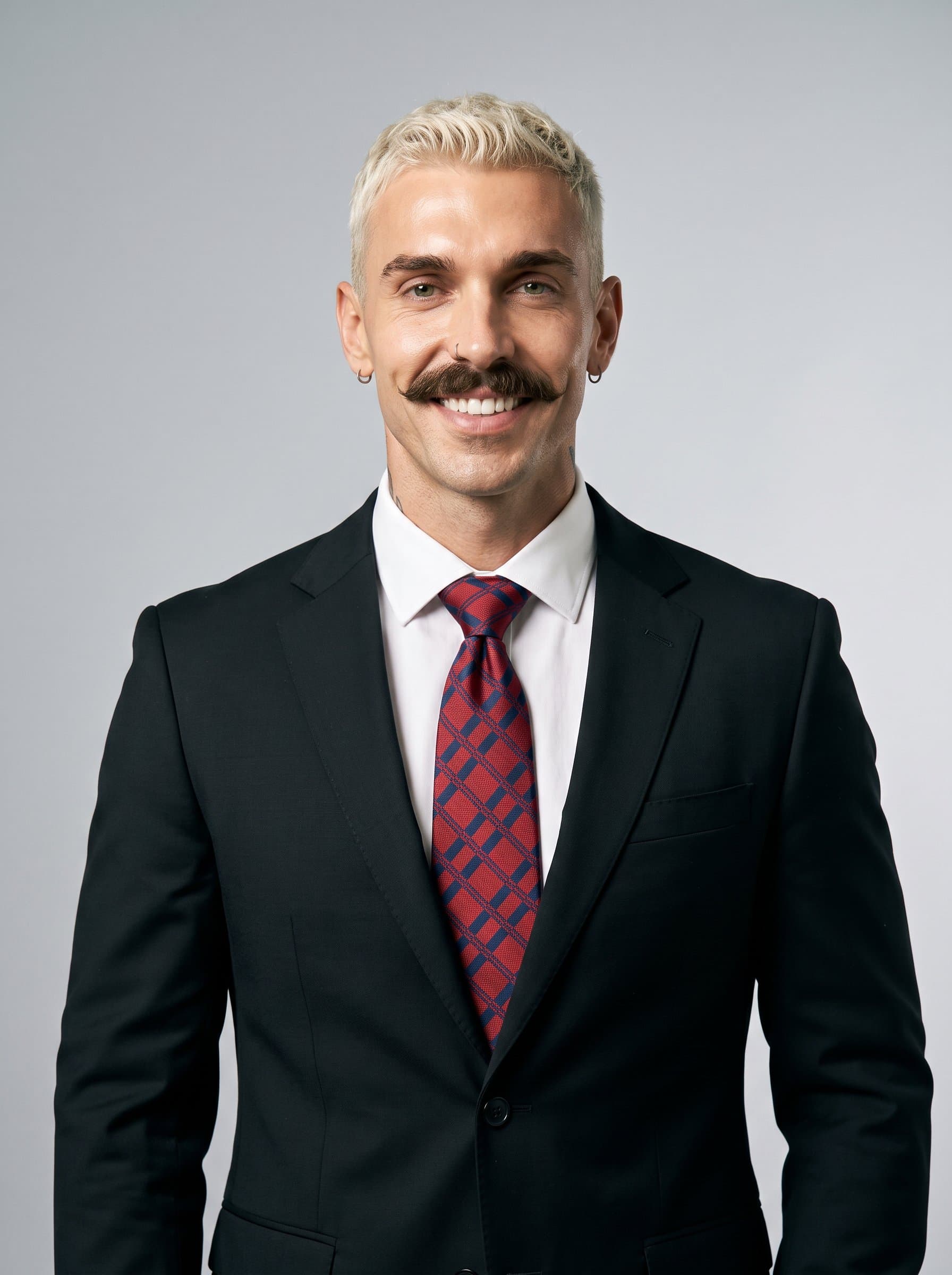 : Consultant headshot featuring a man with wavy hair, donning a sharp black suit and bold tie, standing before a neutral gray backdrop, highlighting a decisive and approachable professional presence.