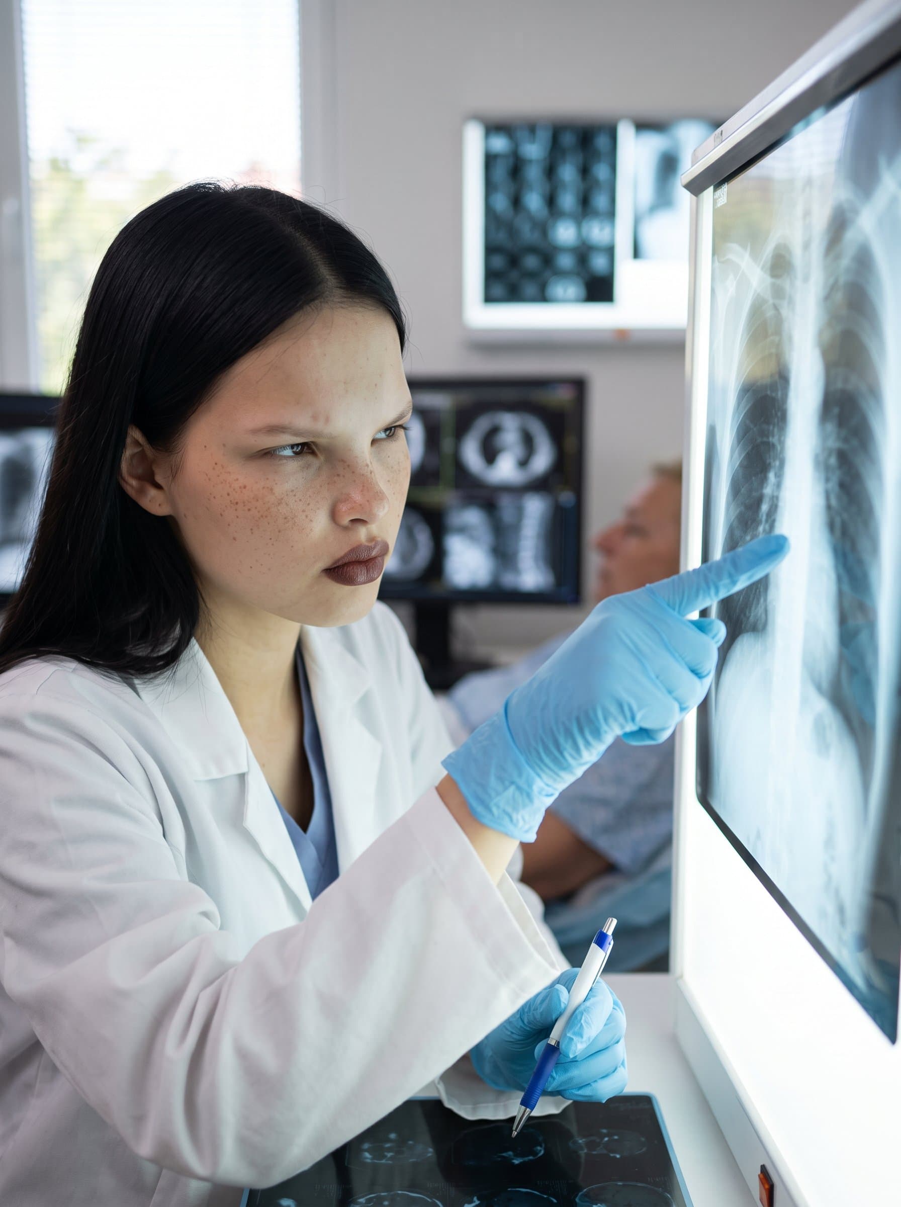 : Portray a healthcare worker with a focused expression, wearing gloves and examining a patient's X-ray against a lightbox, in a radiology lab, capturing precision and acute attention to detail.
