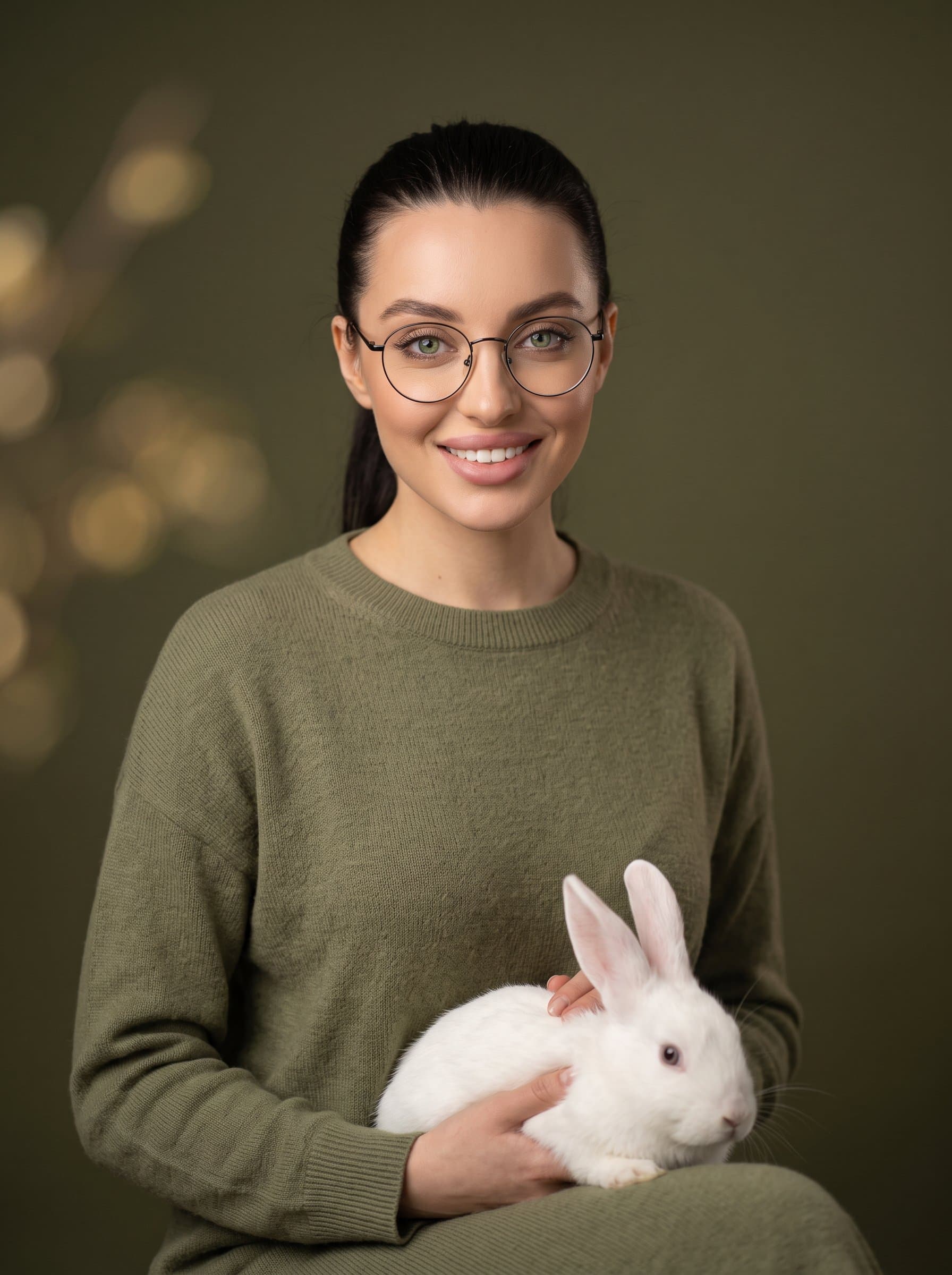 woman wearing round glasses and a neat ponytail, dressed in a minimalist sweater. Background is a muted olive tone, providing a serene and professional vibe. Focus on clear and friendly facial features.