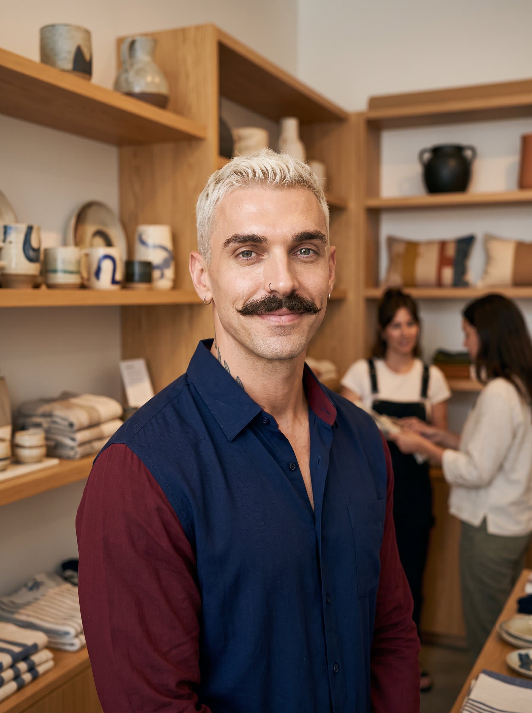 Design an AI-generated headshot with of a retail associate, exhibiting a soft smile and casual blouse, positioned in a chic shop corner emphasizing warmth and accessibility to clients.